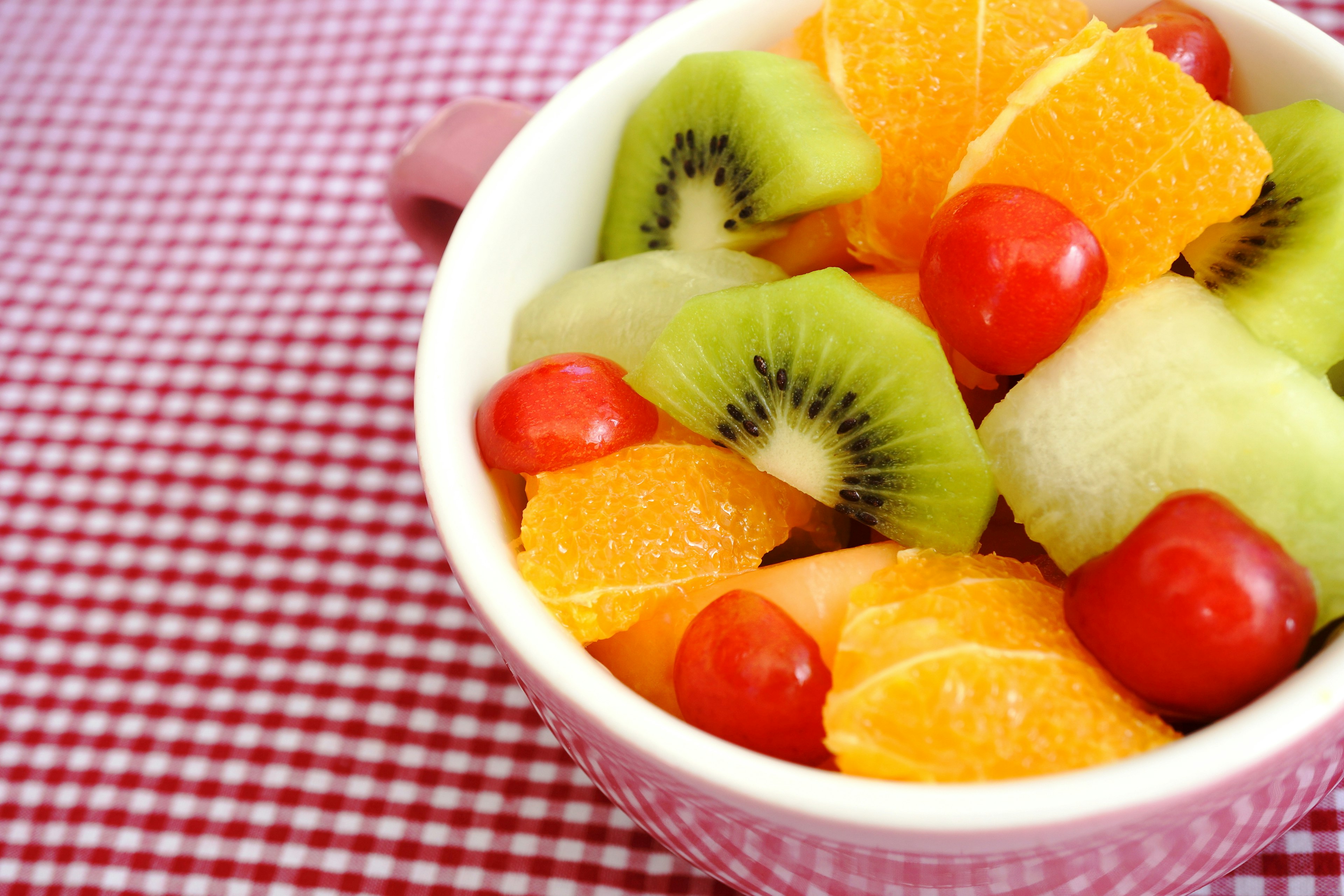 A bowl of fruit salad featuring kiwi, orange, melon, and cherry tomatoes