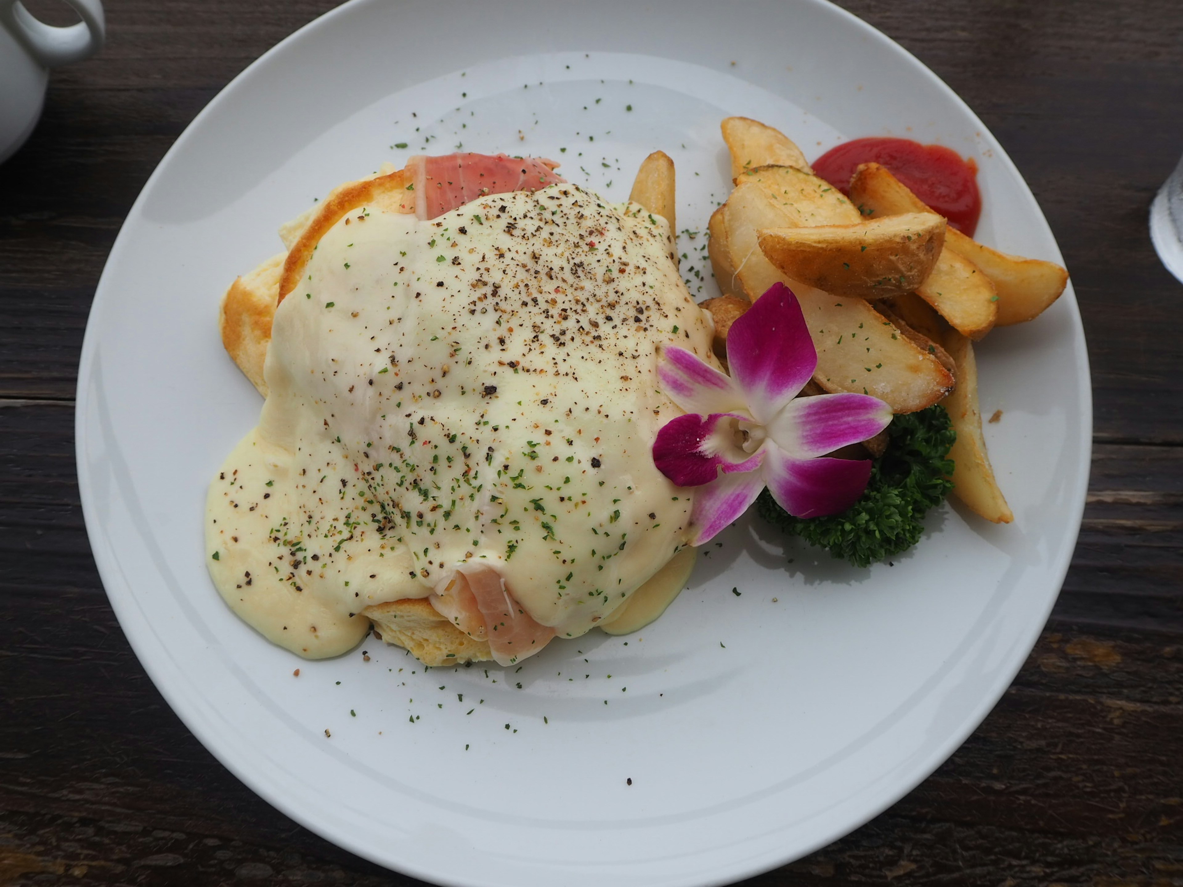 Huevos benedictinos con jamón y salsa cremosa servidos con papas fritas y una flor decorativa