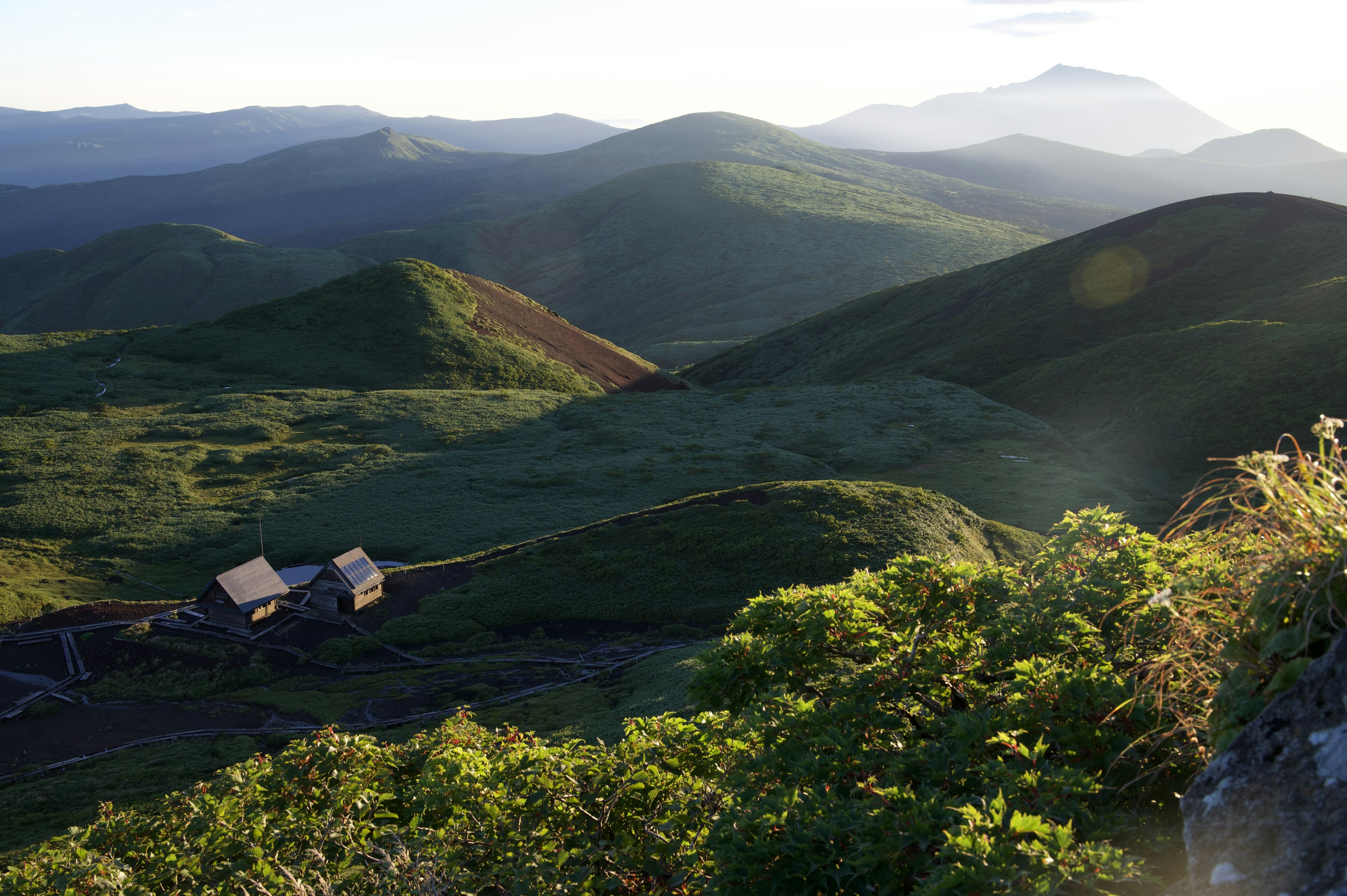 A scenic landscape of rolling hills and mountains with a small cabin