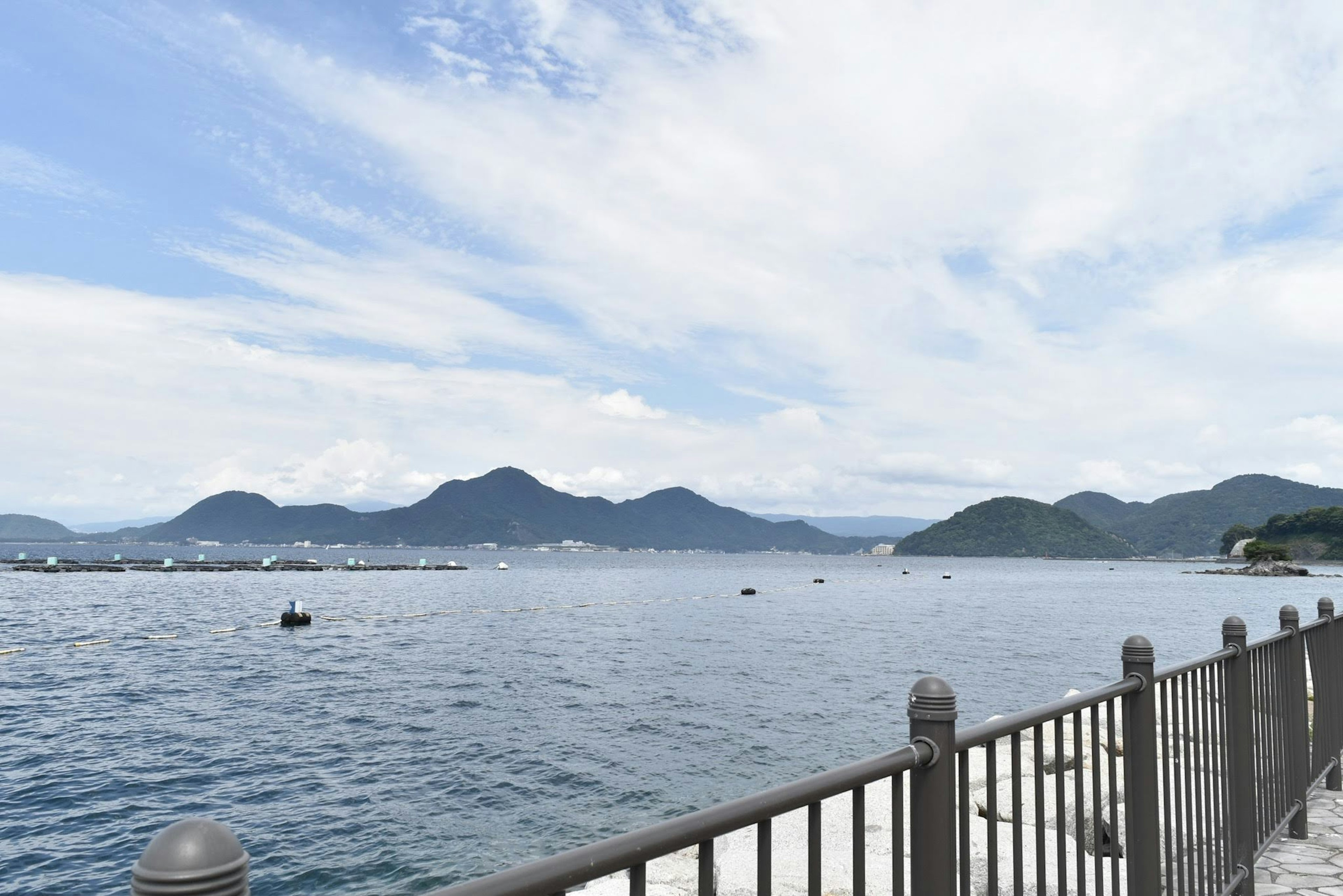 Scenic view of blue sea and mountains along a fence