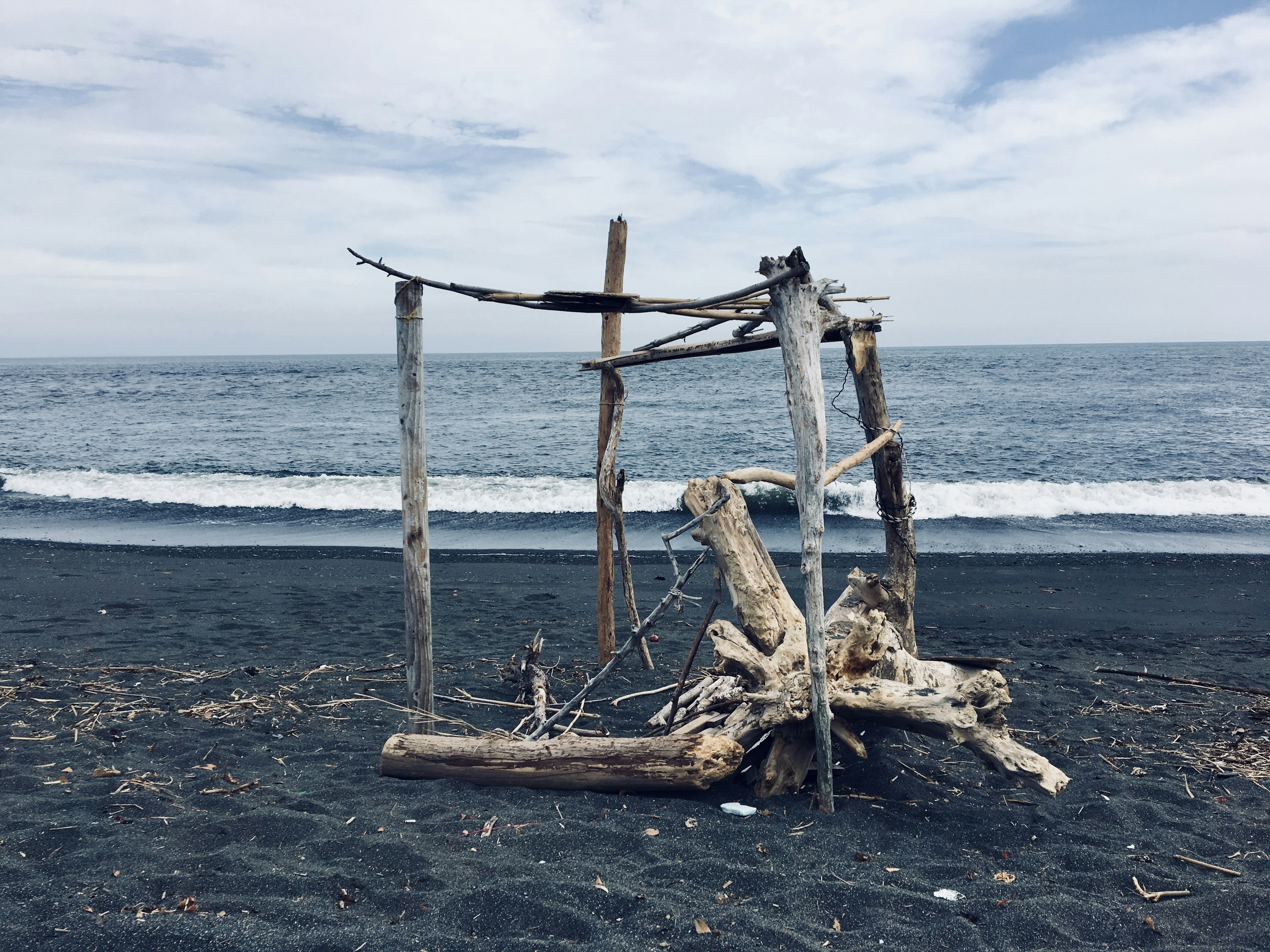 Wooden driftwood structure on a black sand beach with ocean view