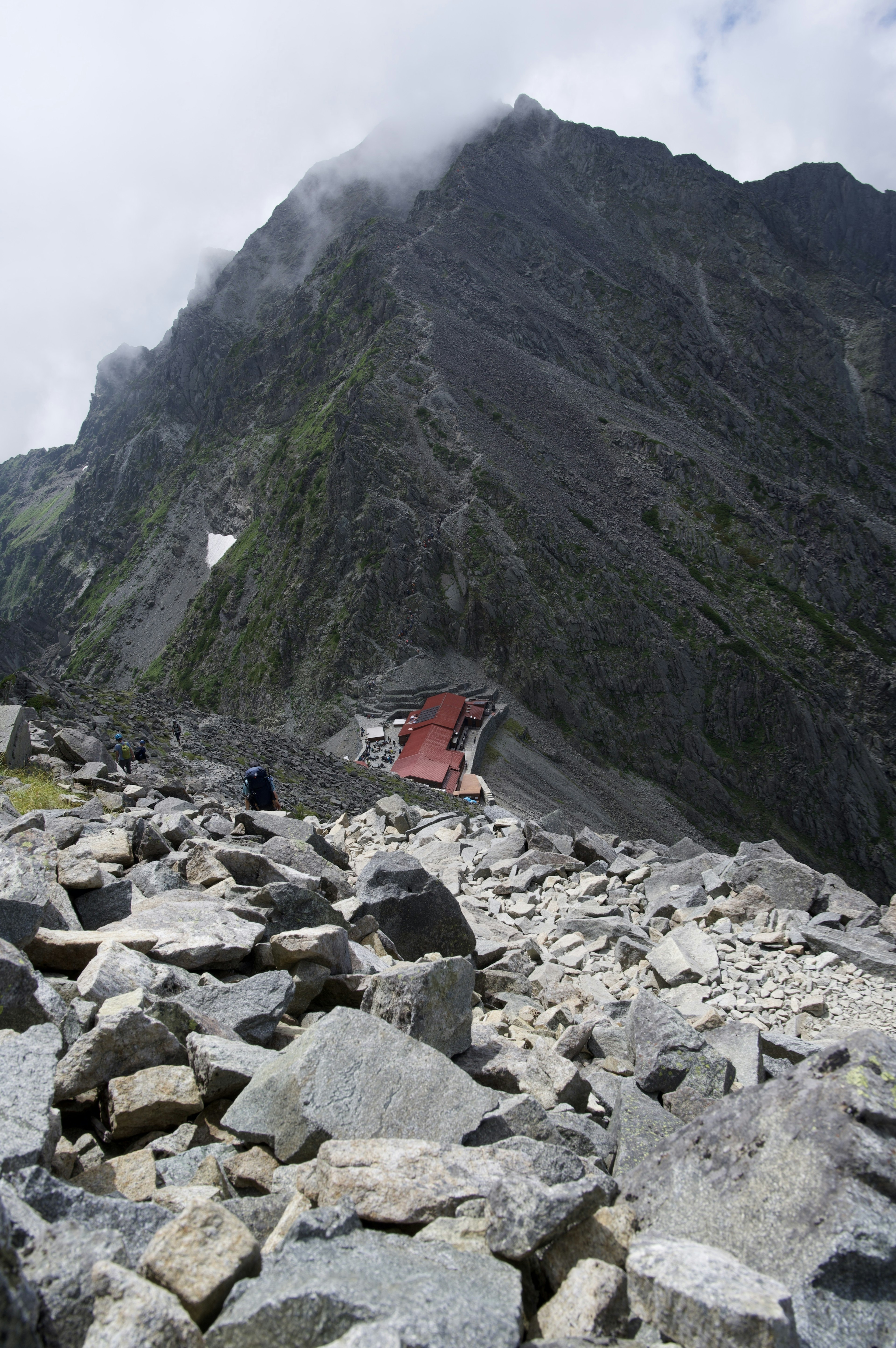 Un paesaggio roccioso con un edificio rosso sul versante della montagna e massi circostanti