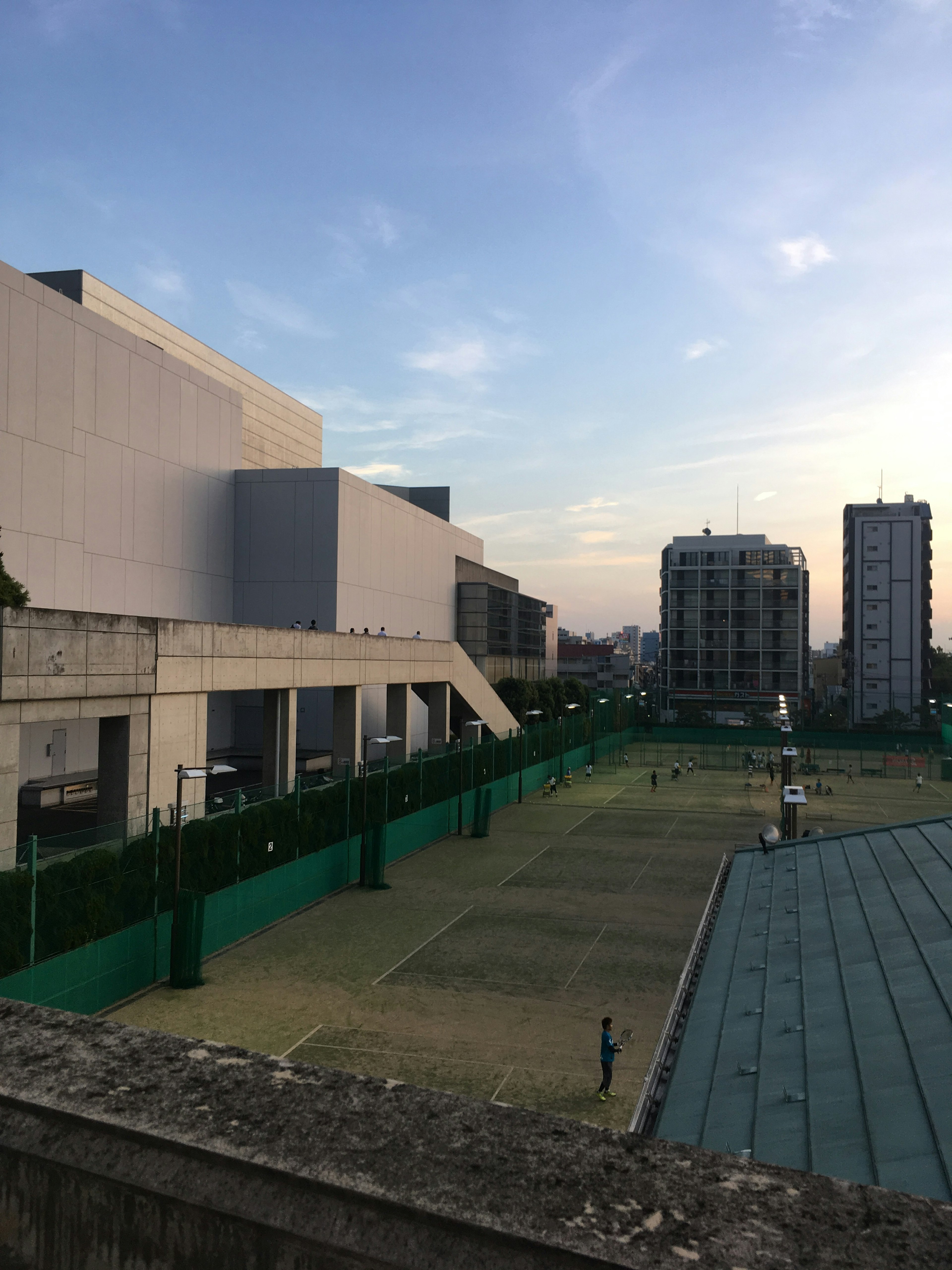 夕焼けの下に広がるテニスコートと現代的な建物の景観