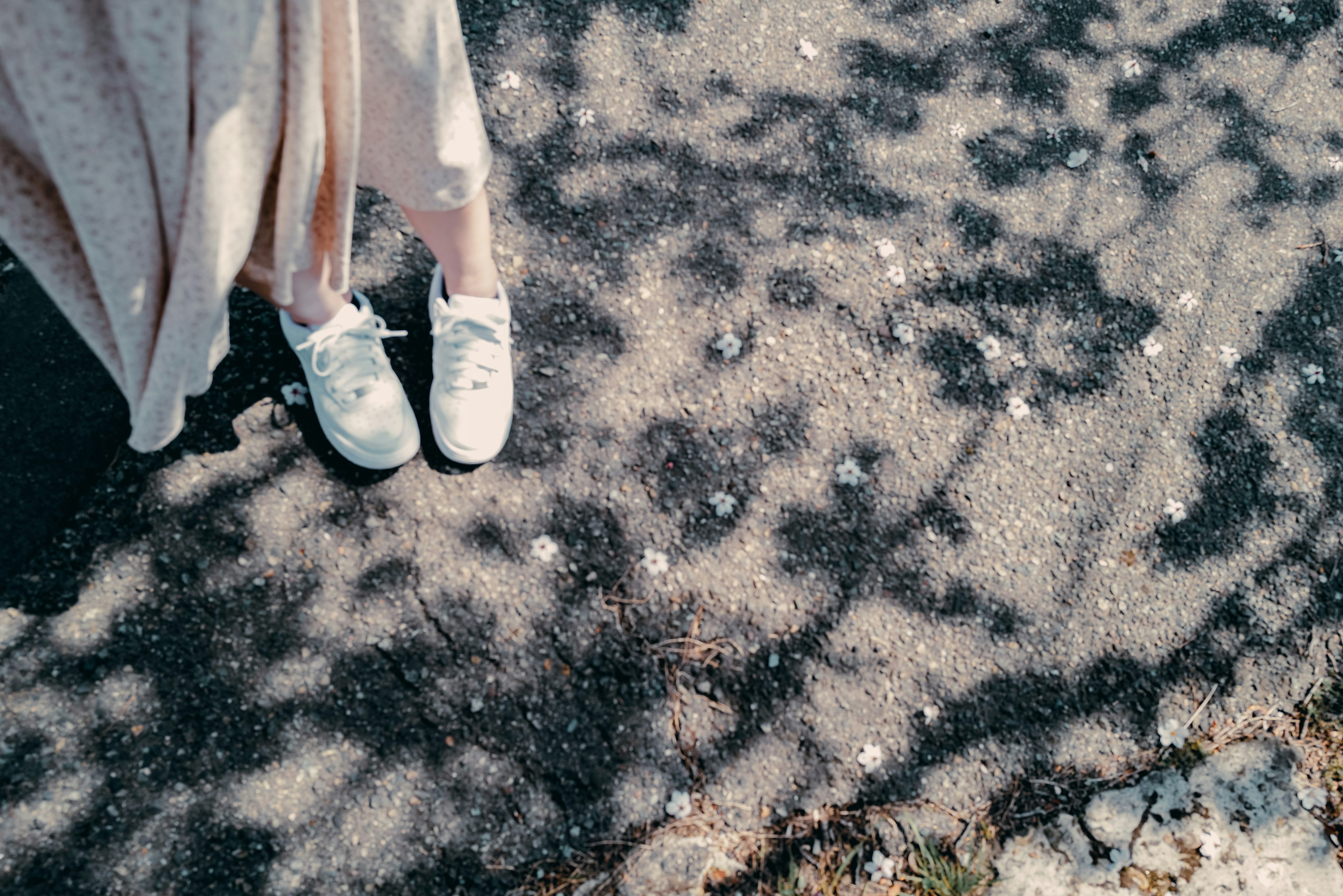 Feet in white sneakers on a paved path with shadow patterns