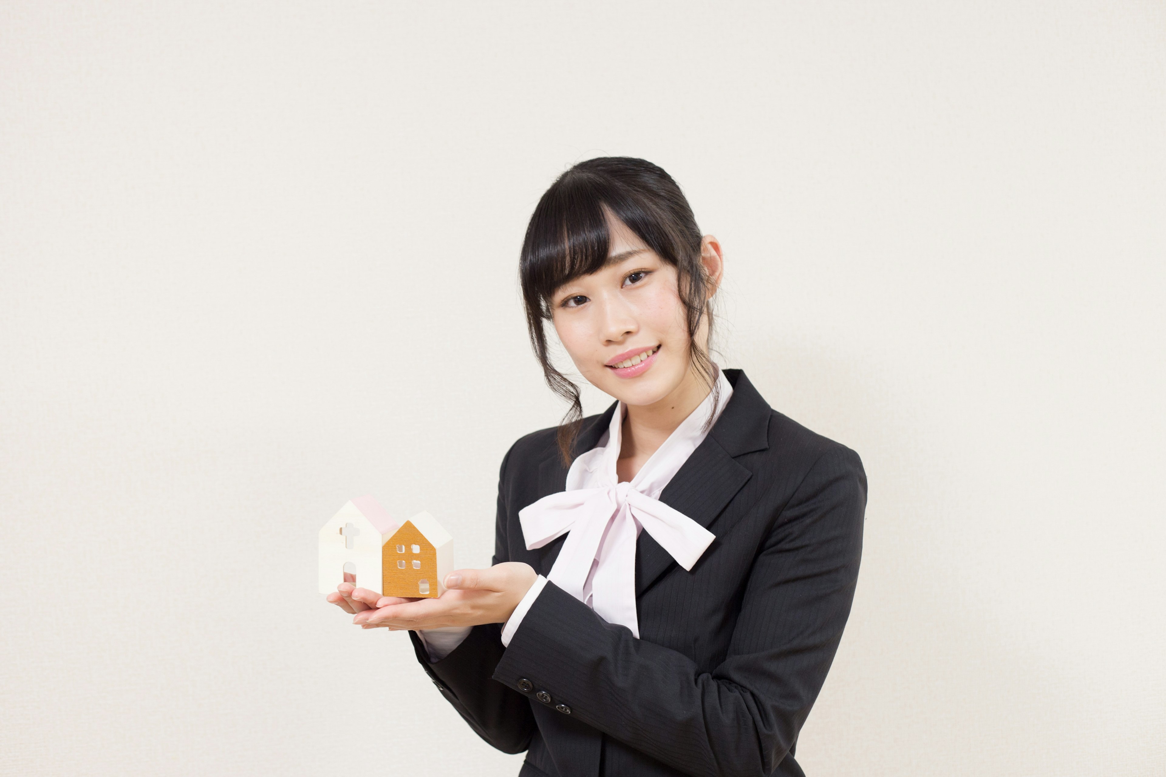 A woman in a business suit holding miniature house models and smiling