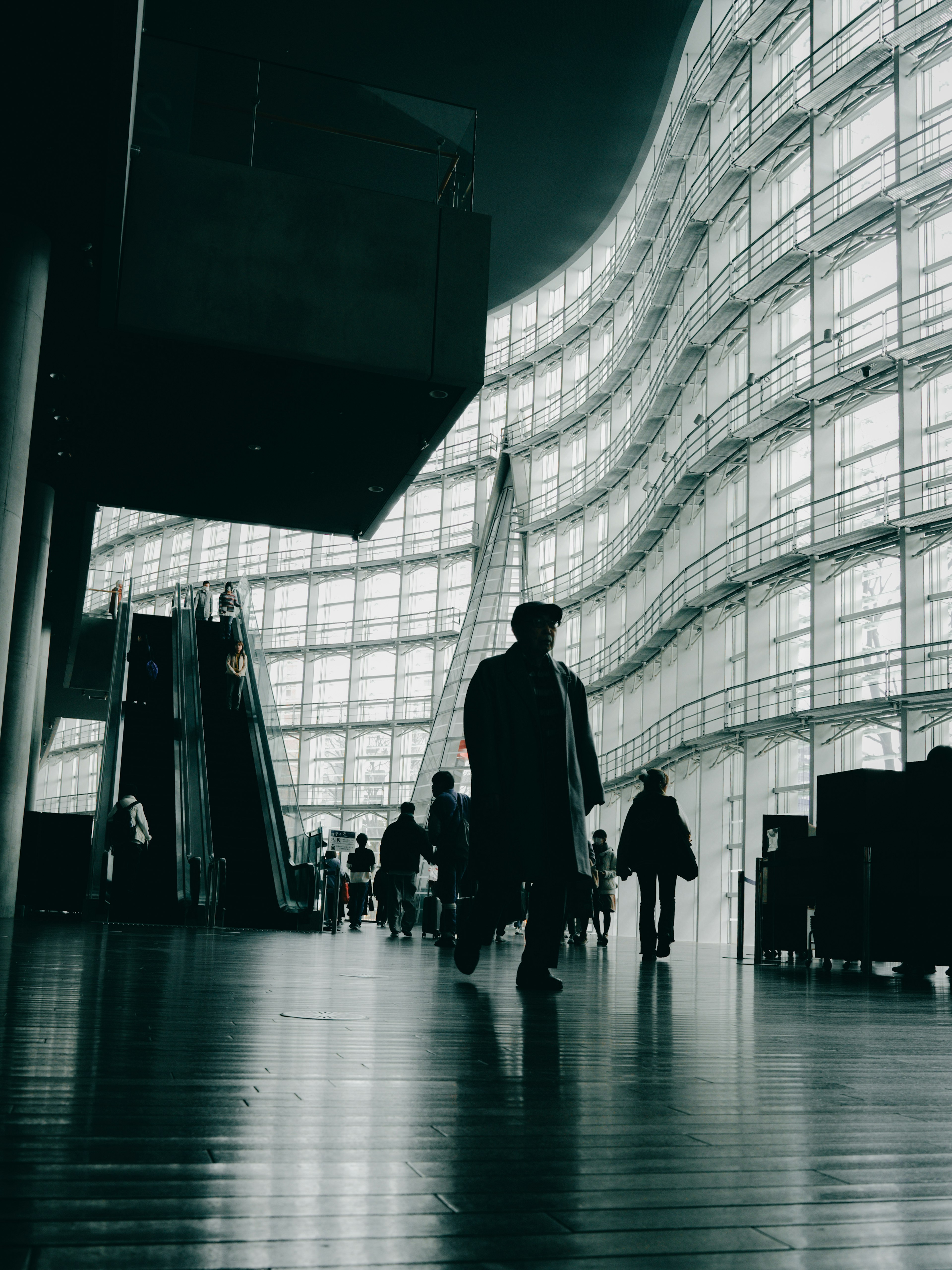 Silhouettes of people walking inside a modern building with a curved glass facade