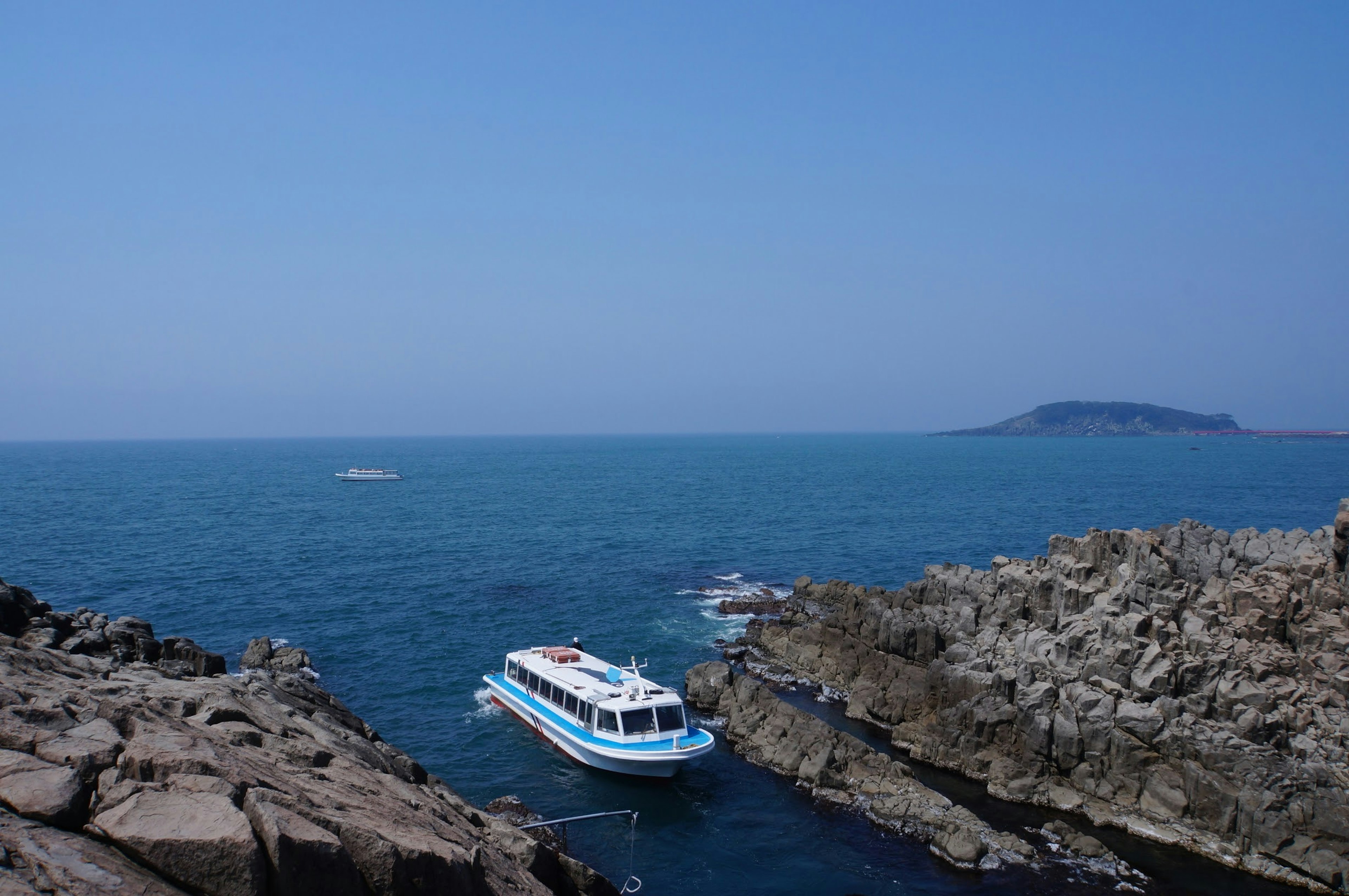 藍色海洋中漂浮的白藍相間的船和岩石海岸