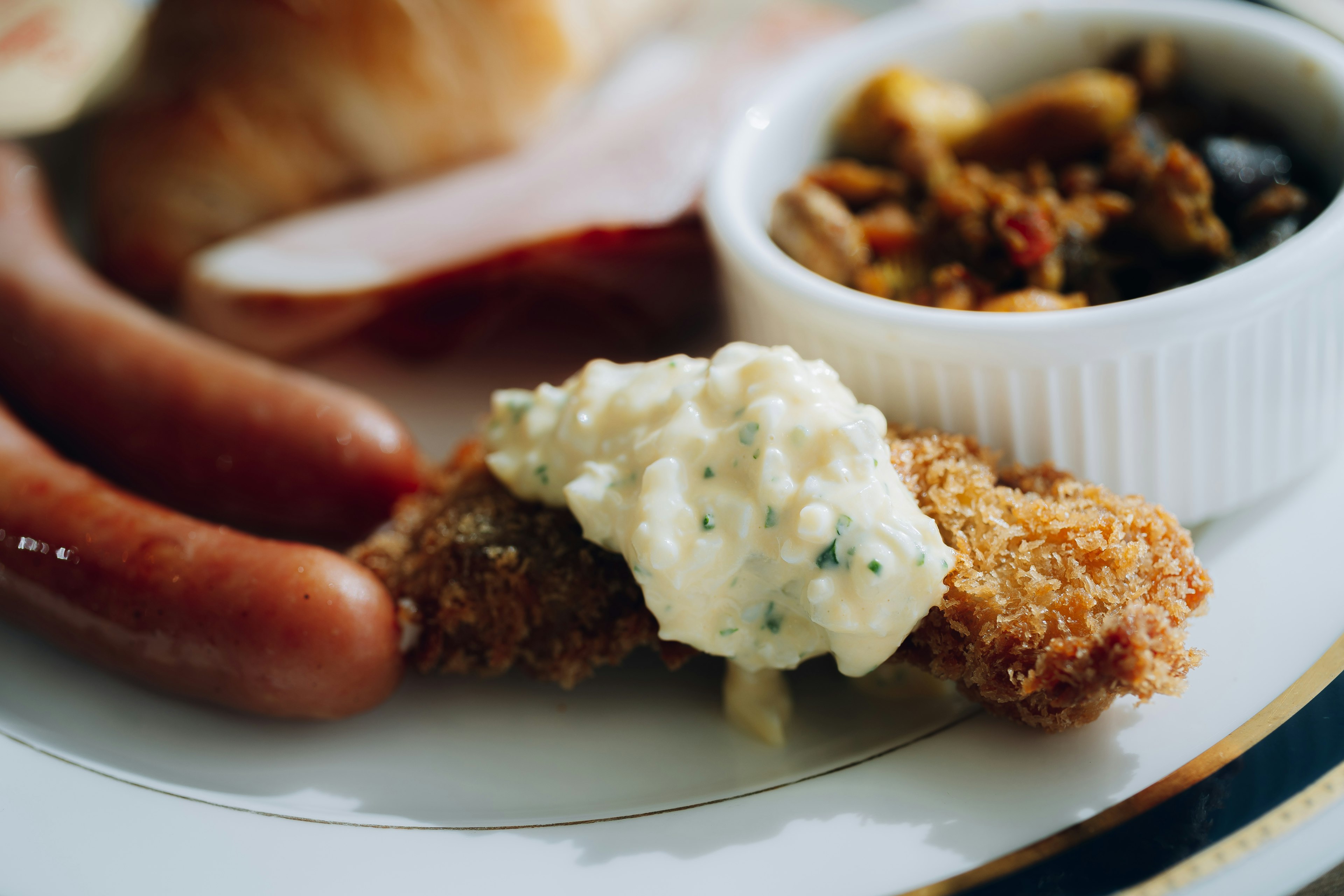 Plato de pollo frito con salsa cremosa junto a salchichas y rodajas de salami