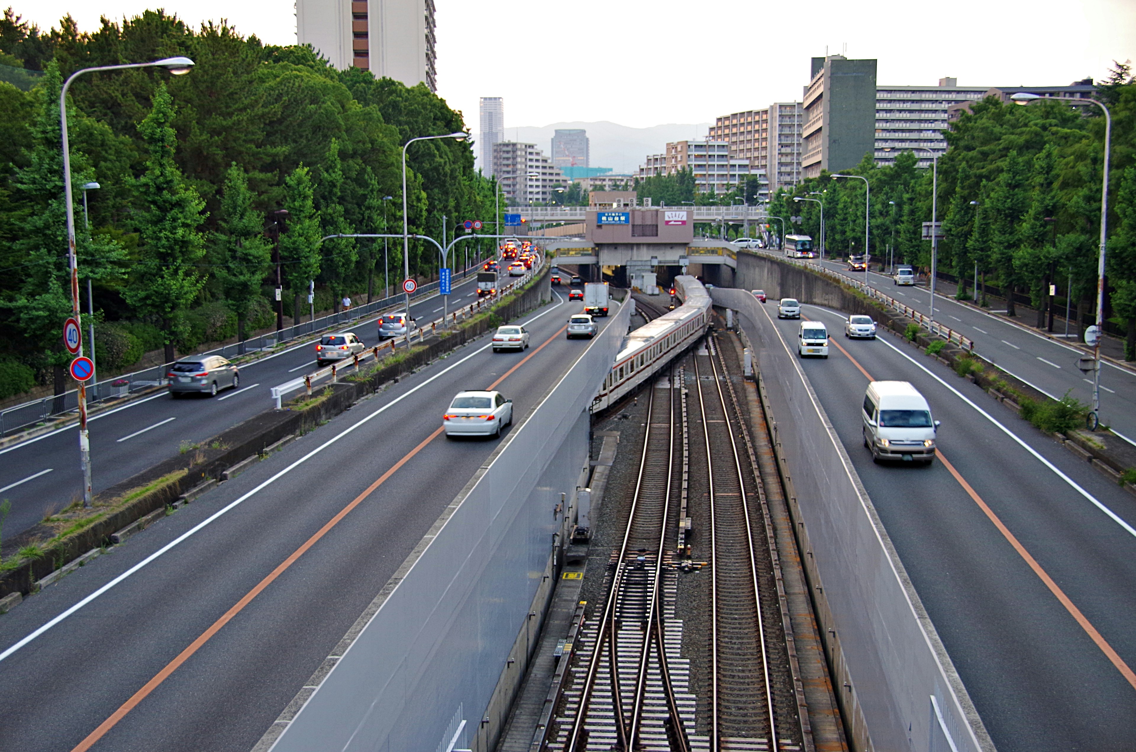 Urban scene featuring an elevated roadway intersecting with railway tracks surrounded by greenery and buildings