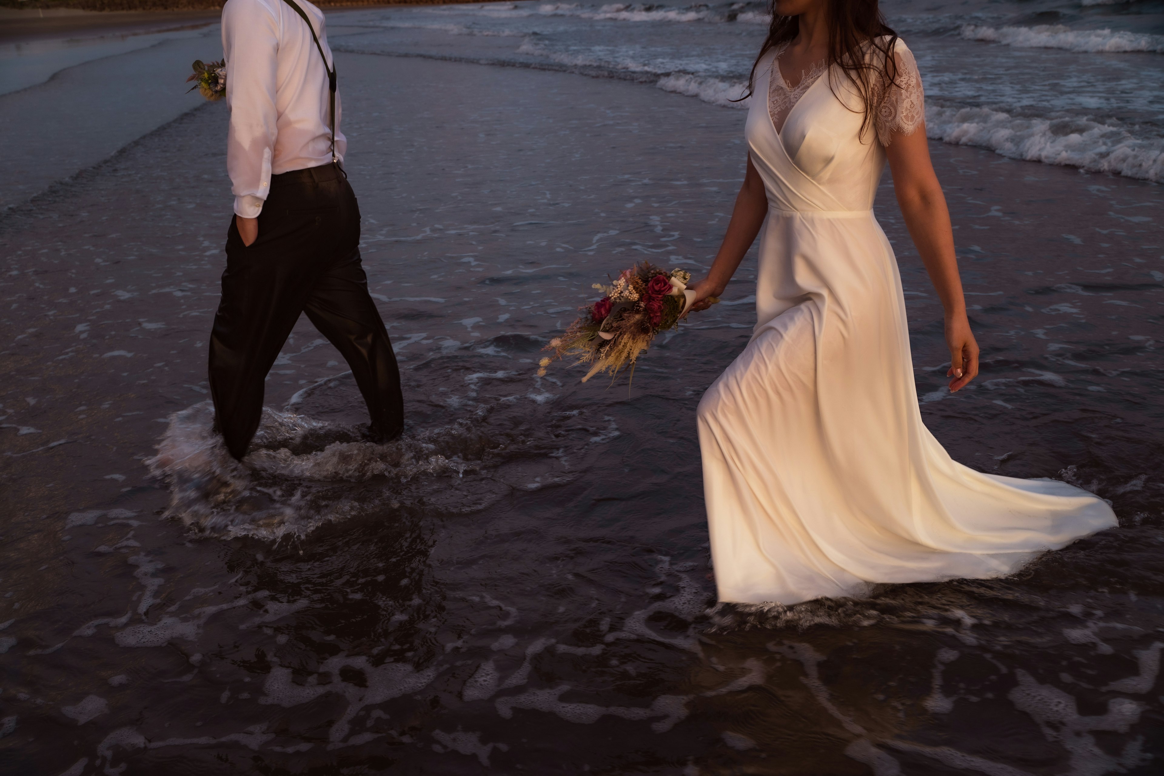 Una donna in abito bianco e un uomo in pantaloni neri che camminano nell'acqua sulla spiaggia