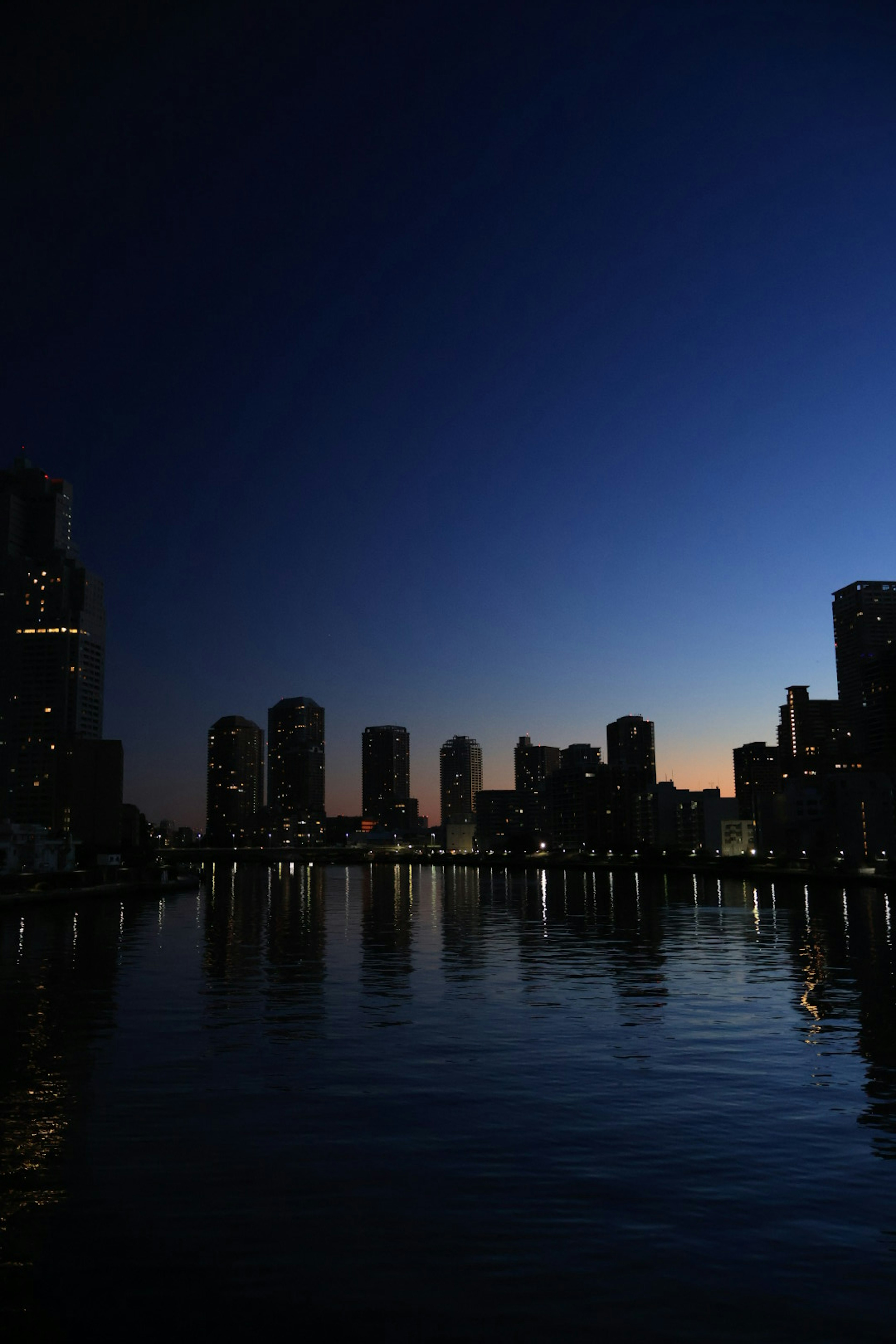 Silhouette of city skyline at dusk with calm water reflections