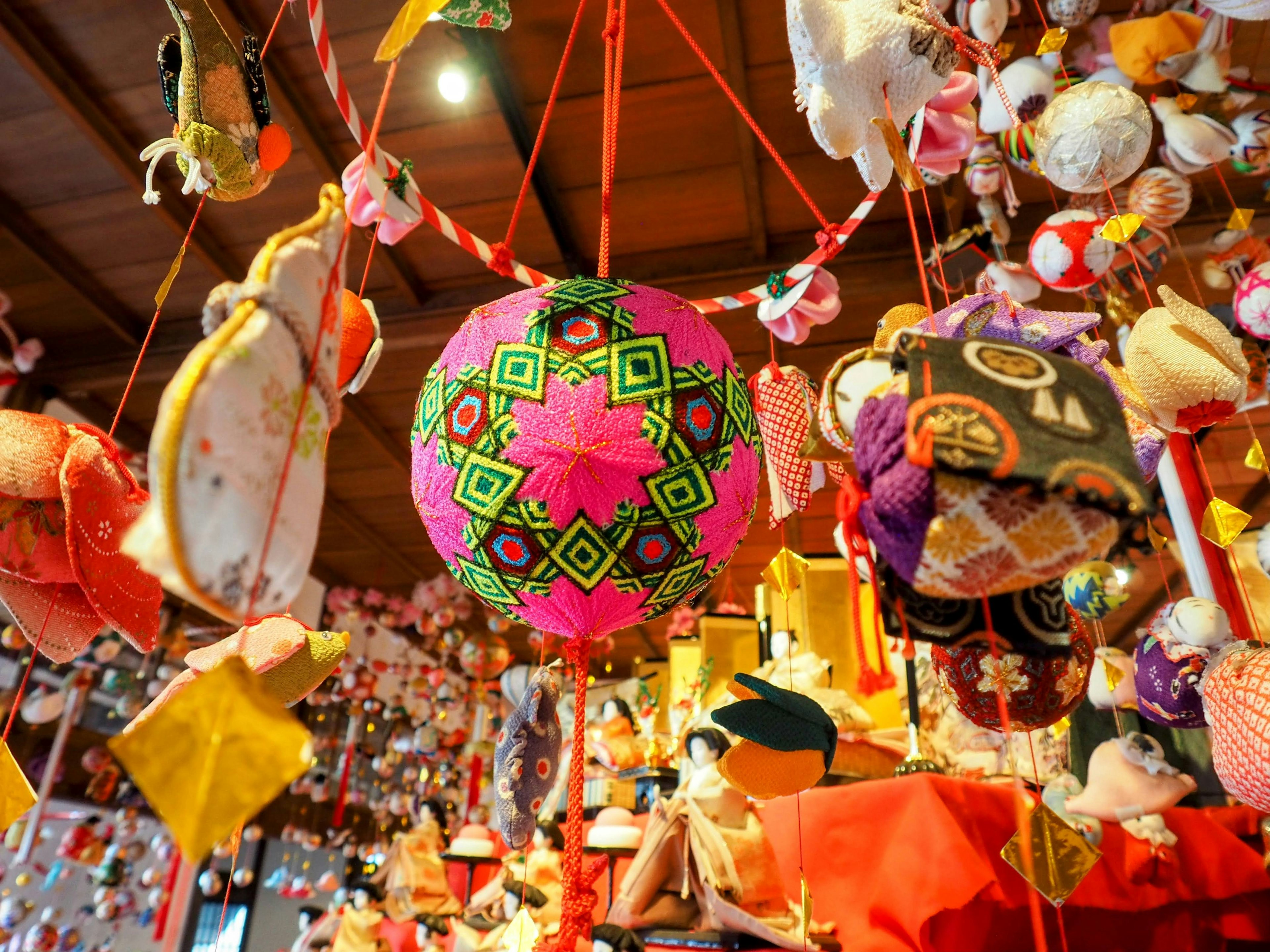 Colorful hanging dolls displayed indoors with a central pink decorative ball surrounded by traditional Japanese dolls and ornaments