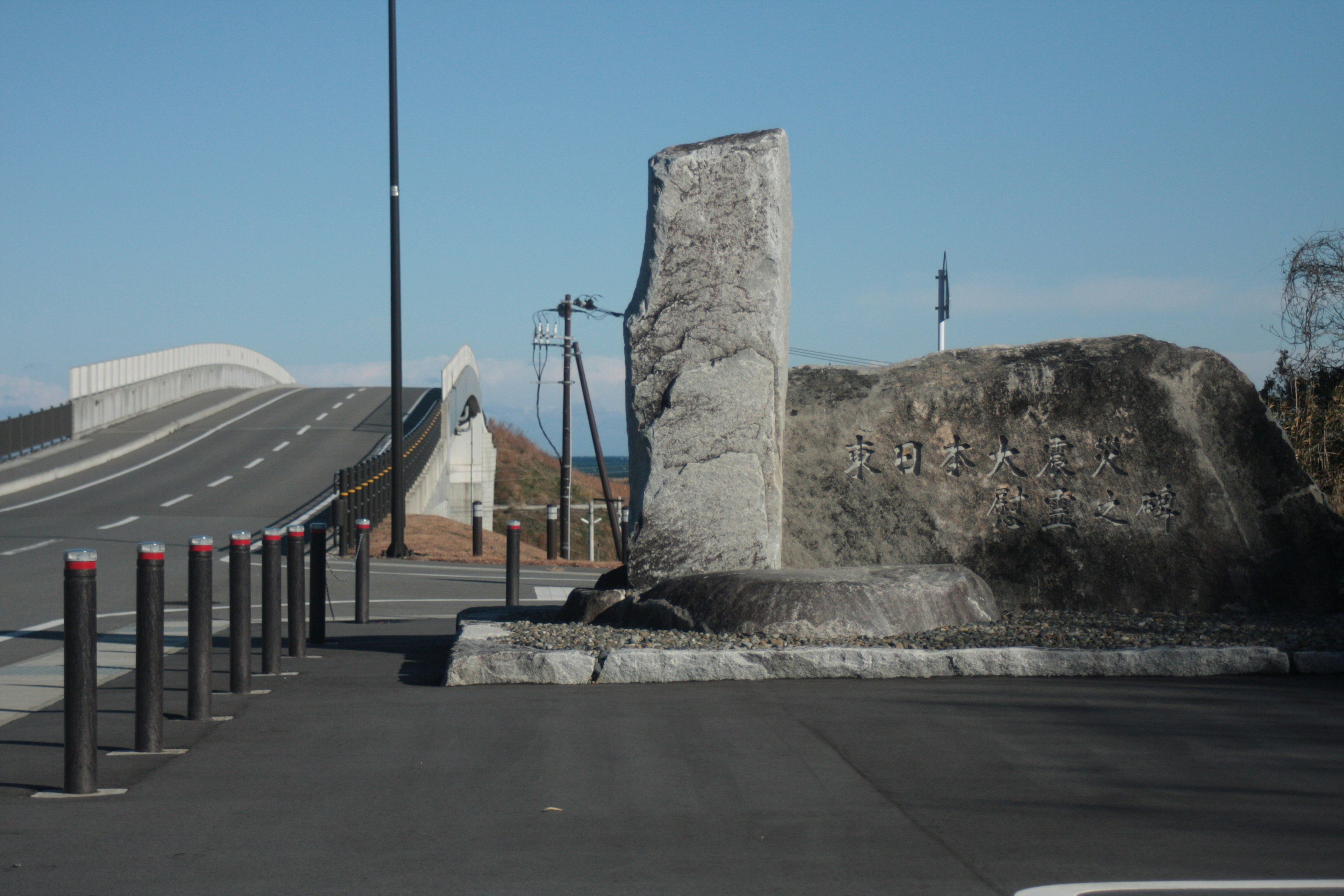 Un grand rocher à côté d'une route avec un pont en arrière-plan