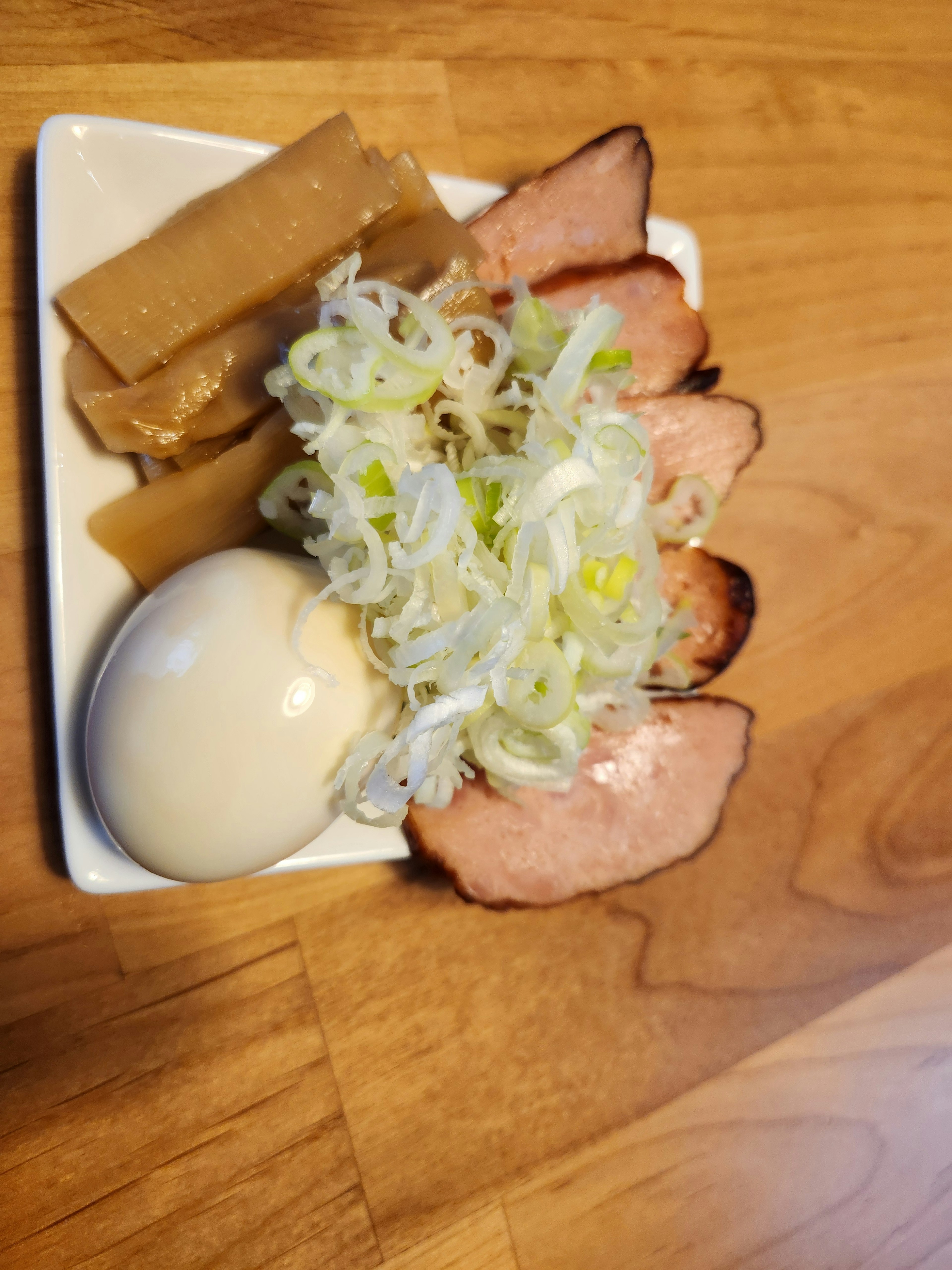 Sliced pork on a white plate with scallions boiled egg and bamboo shoots