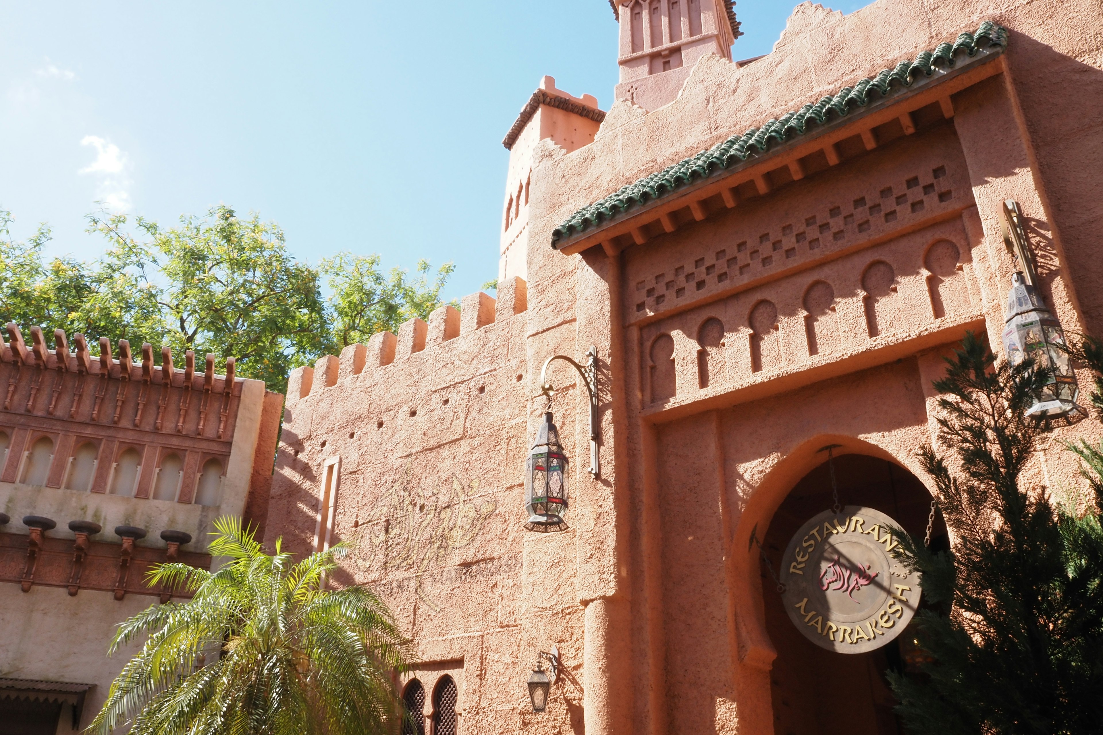 Extérieur d'un bâtiment de style marocain avec des murs roses clairs arche décorative toit vert plantes environnantes