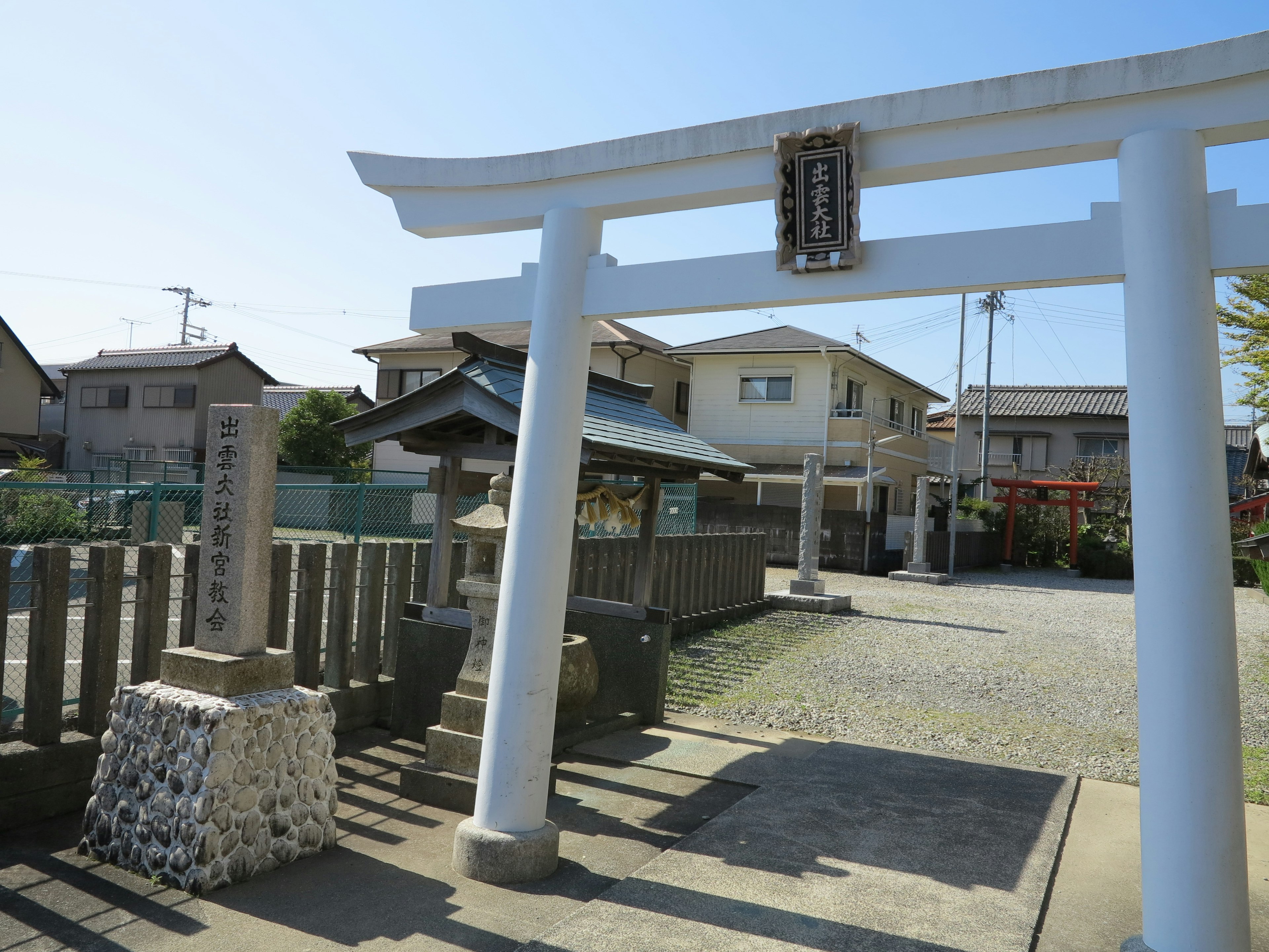 Gerbang torii putih dengan bangunan perumahan di sekitarnya di sebuah kuil