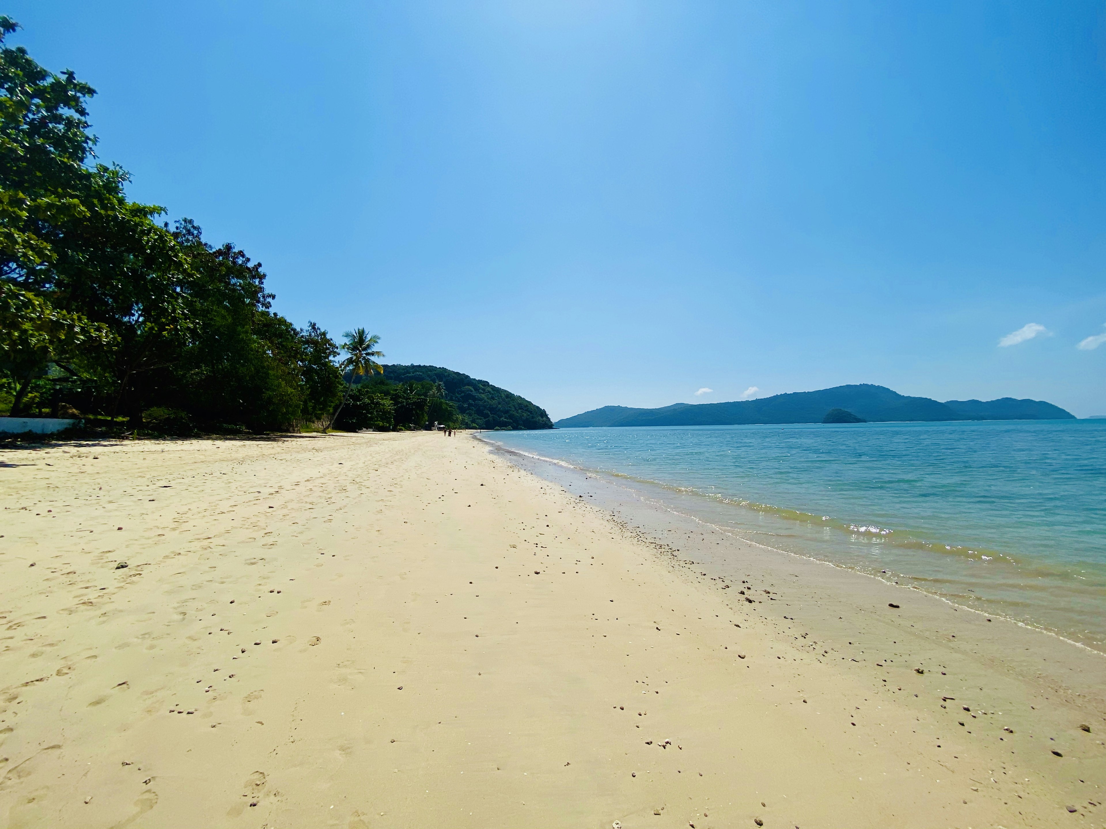 Pemandangan pantai yang indah, langit biru, laut tenang, pohon hijau, pulau-pulau jauh