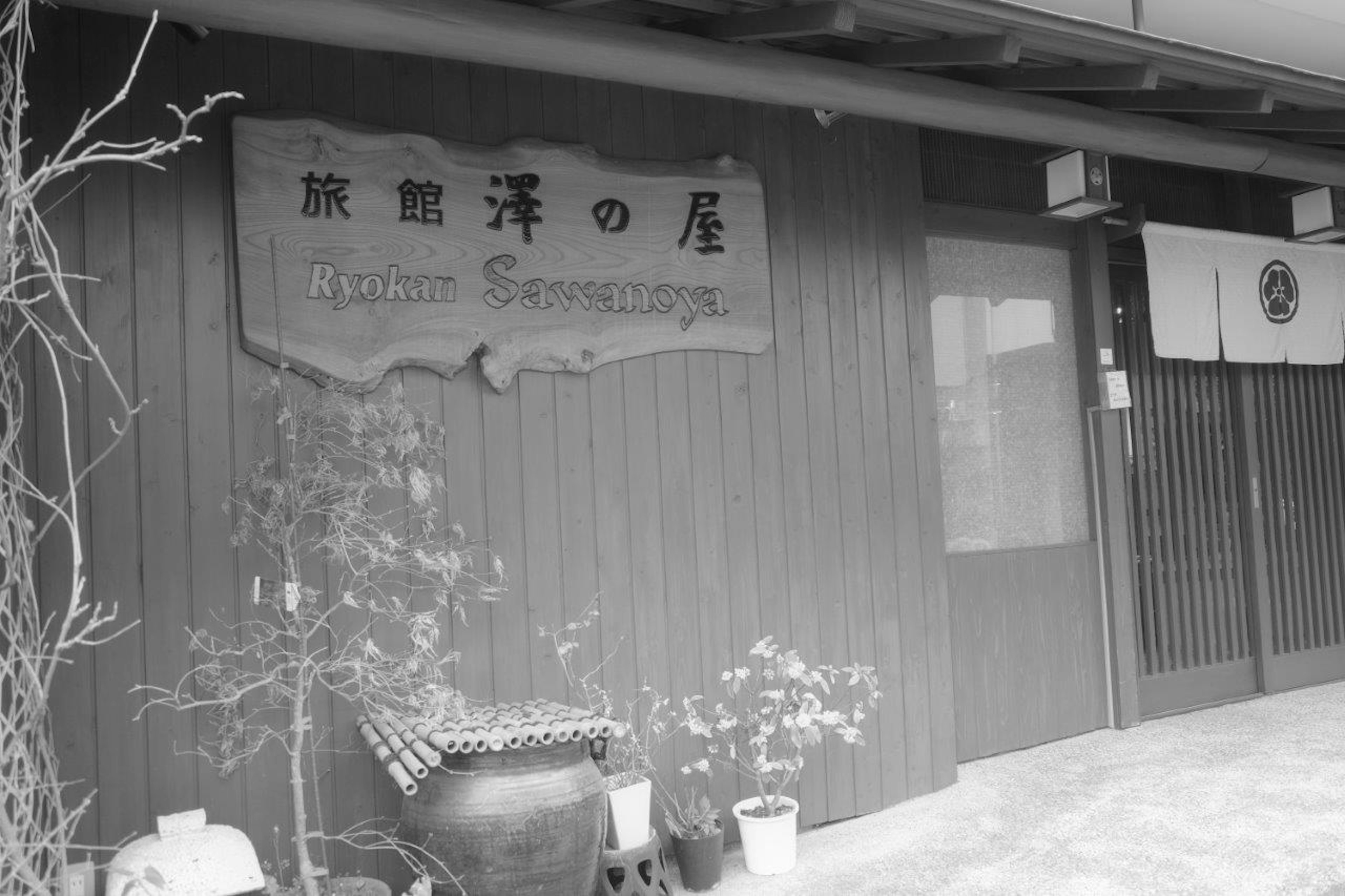 Extérieur d'un ryokan avec une enseigne en bois et des fleurs en pot