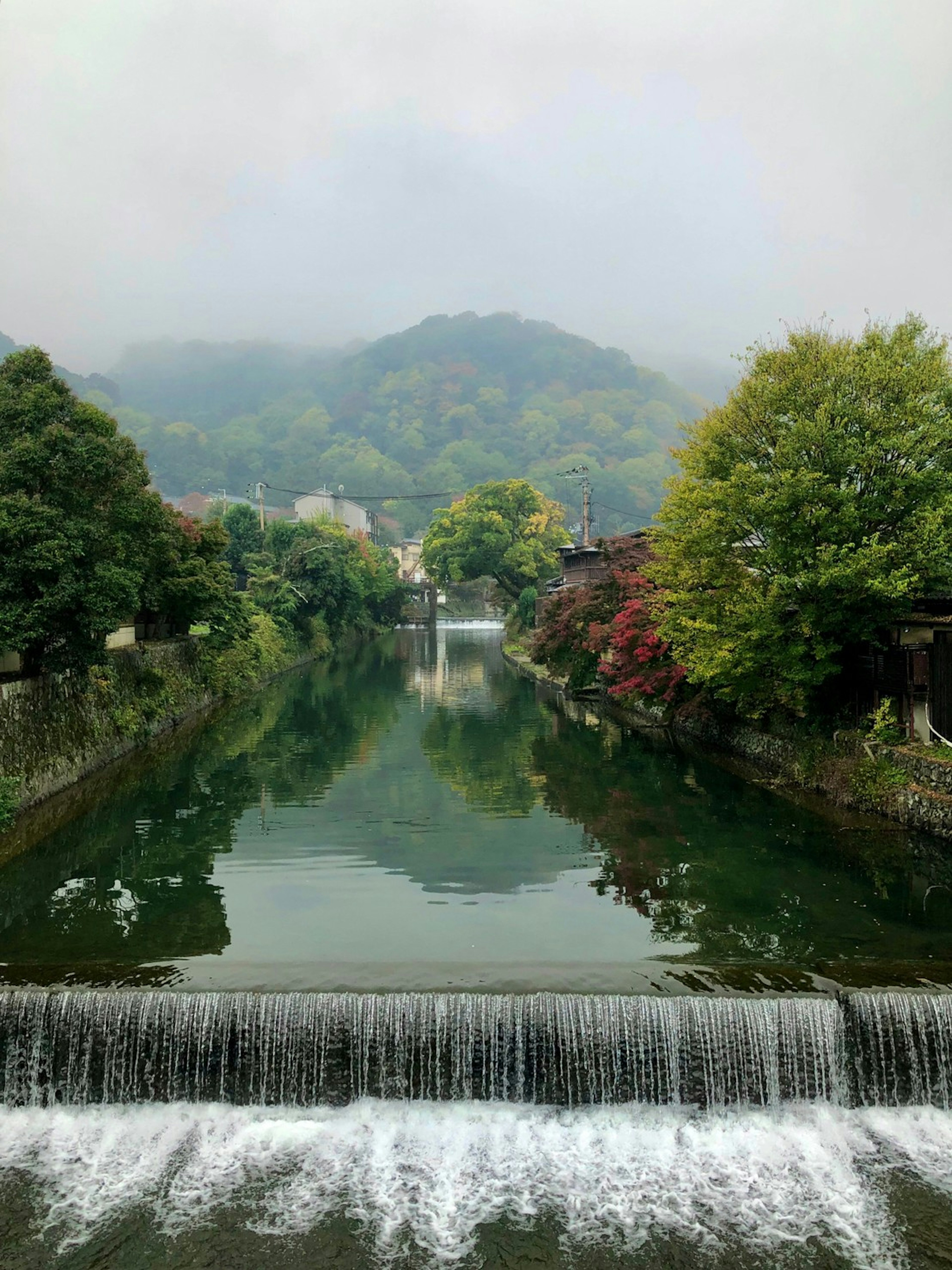 Vista serena del río con cascada árboles verdes y montañas brumosas