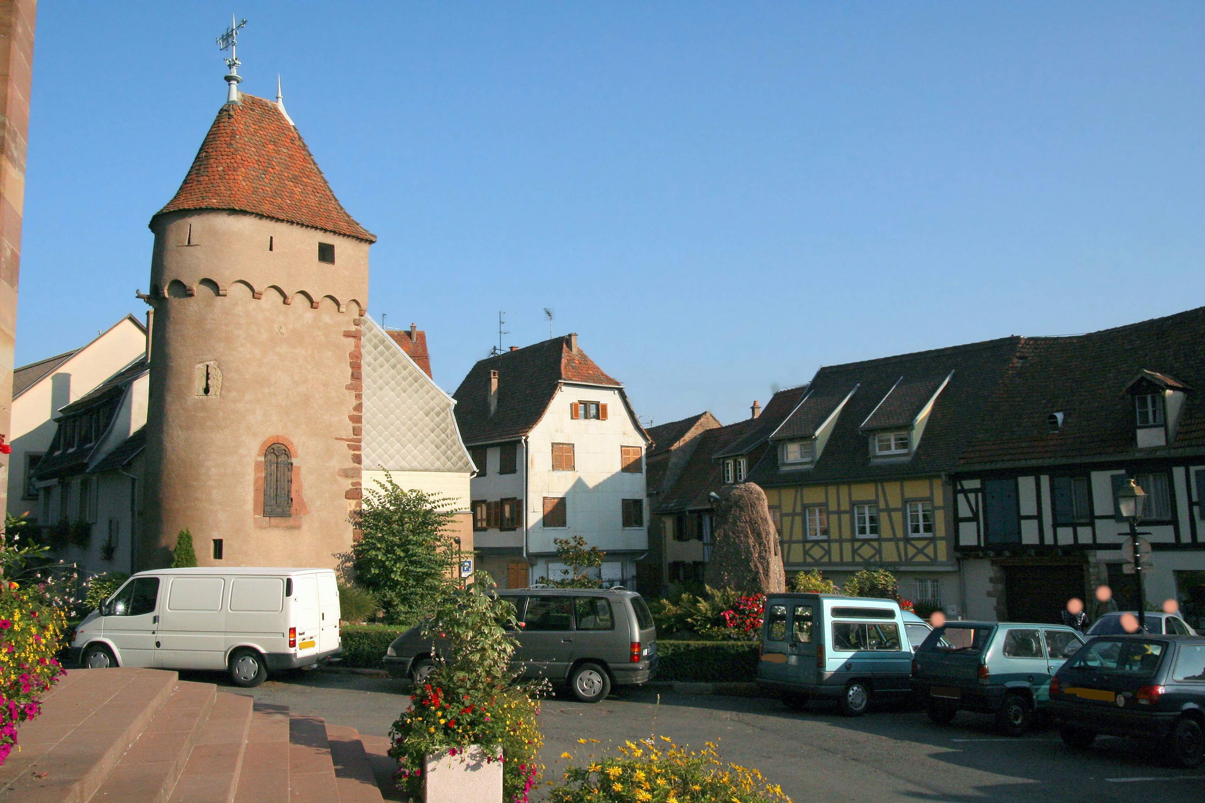 A square in a French village featuring a medieval tower and historic buildings