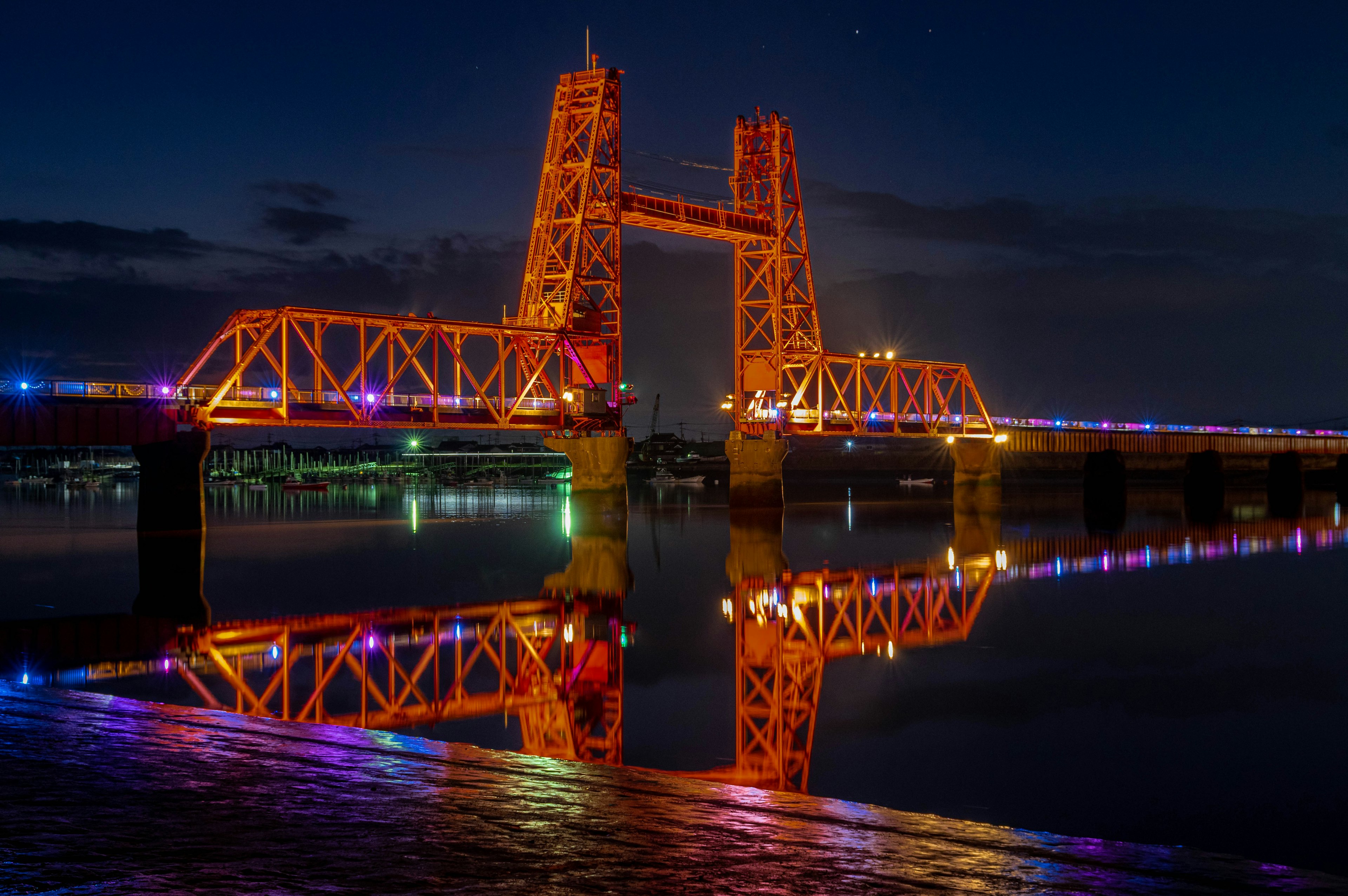 Bridge illuminated with colorful lights reflecting on the water at night