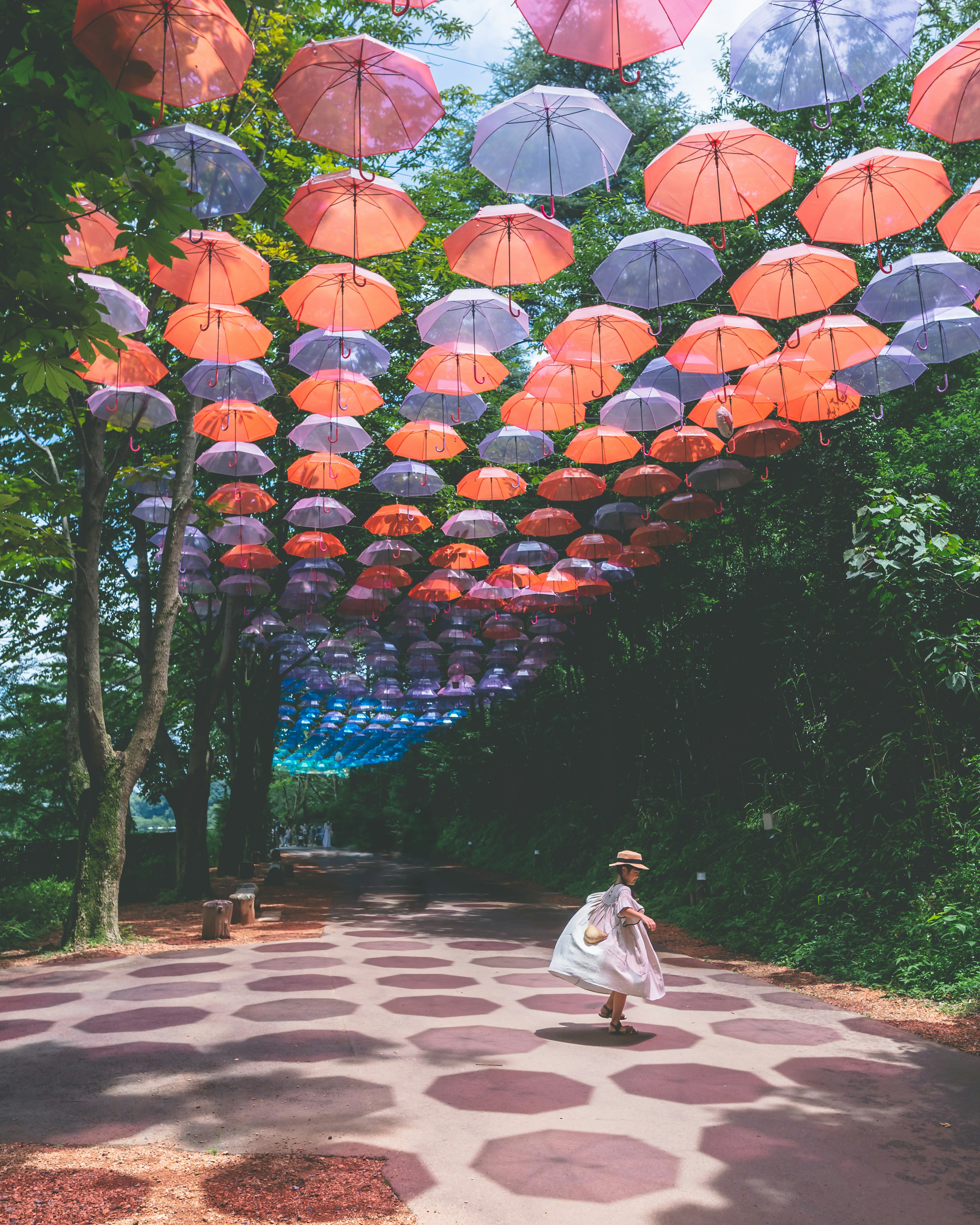 Girl walking under colorful umbrellas in a shaded path