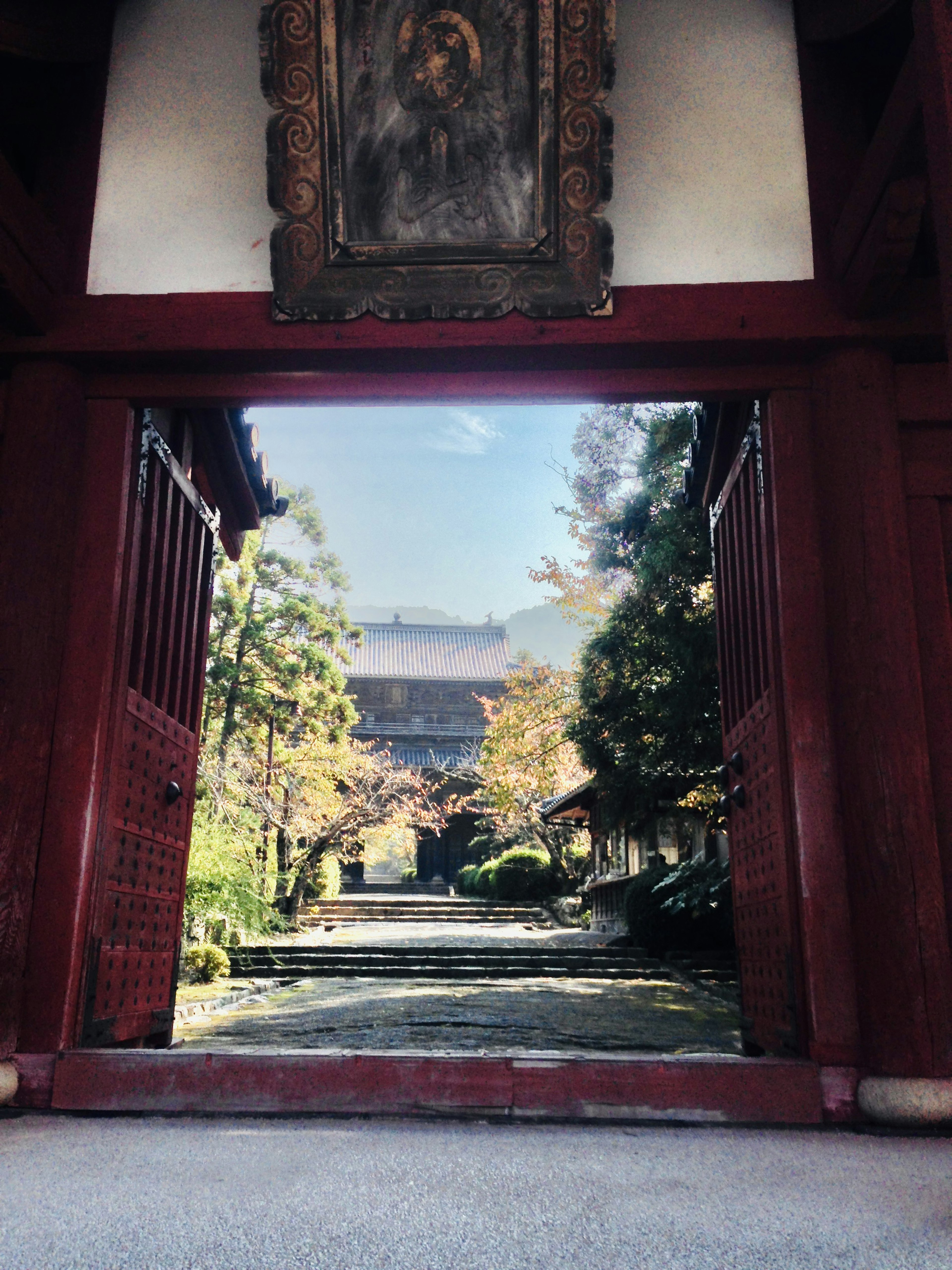 Vista a través de una puerta roja que muestra un jardín y un edificio