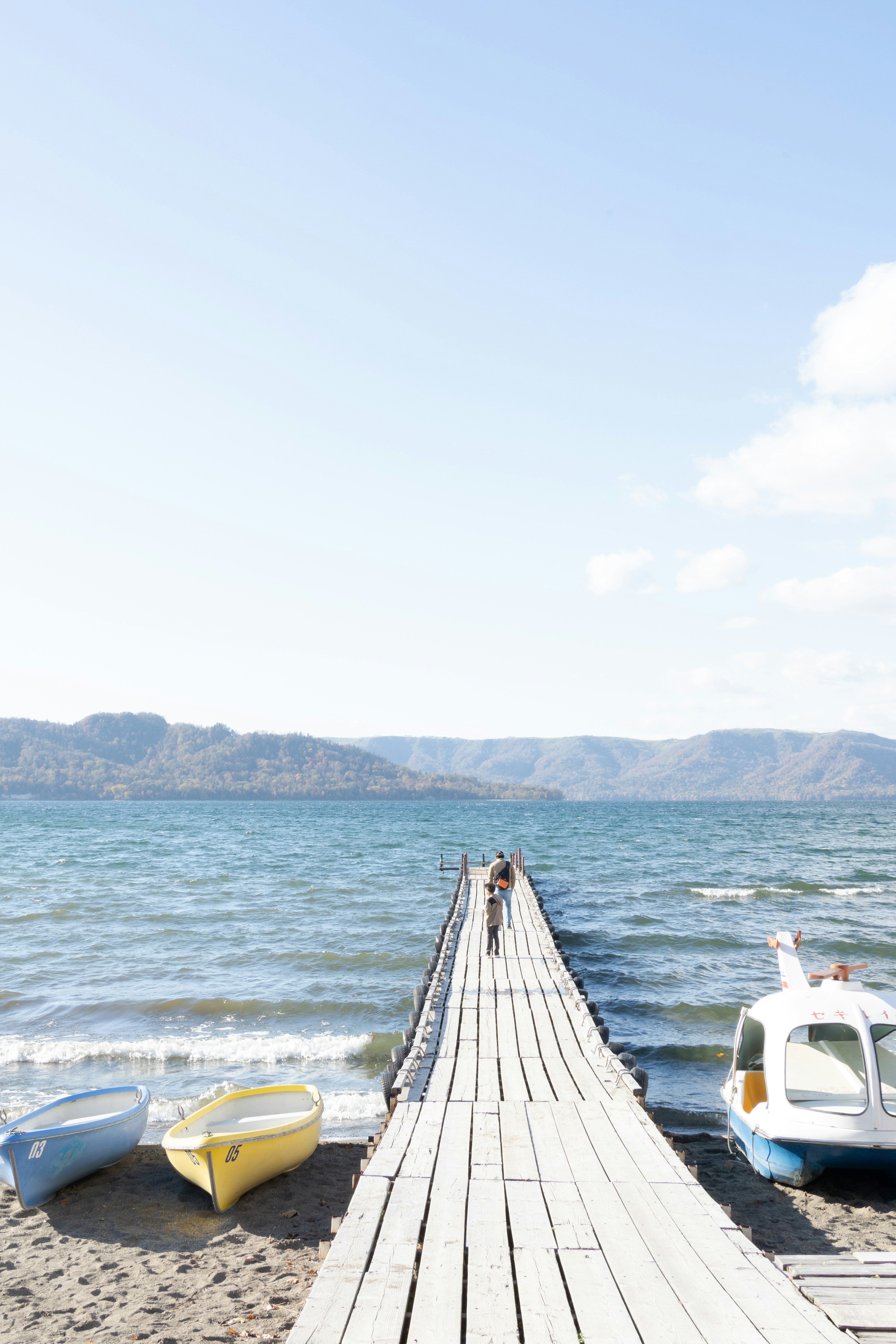 Vista escénica de un muelle de madera que se extiende en agua azul con botes en la orilla