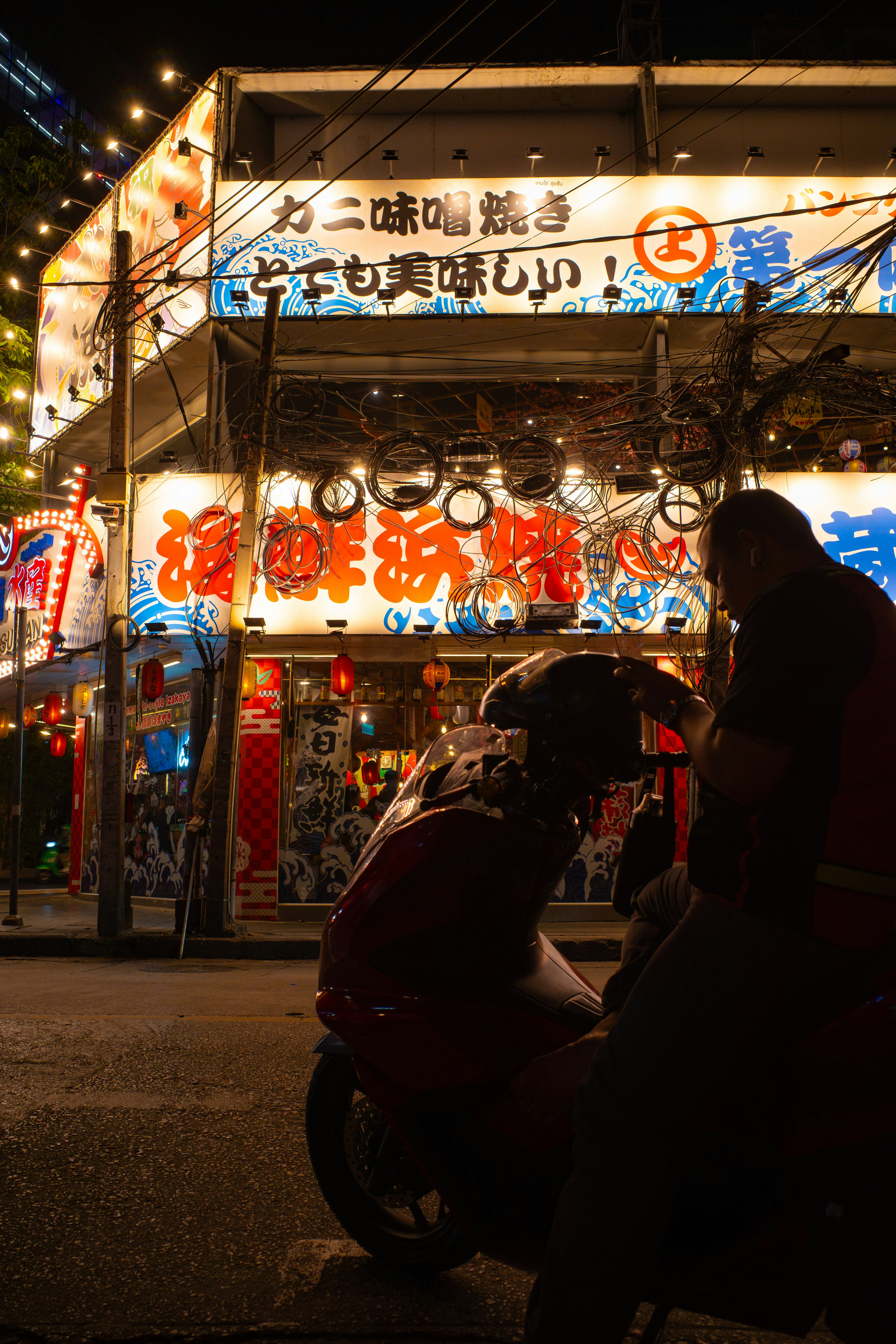 夜の街で明るい看板が輝く飲食店の外観とその前に座る人々