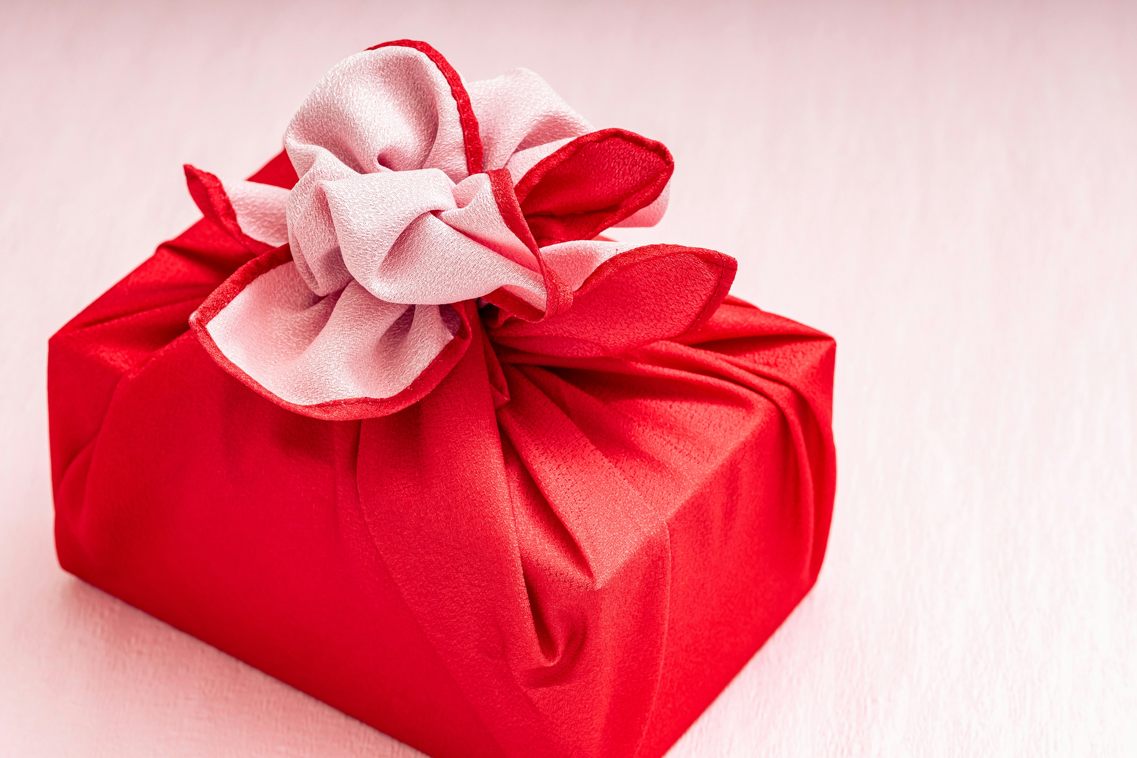 A red gift wrapped in fabric with a white bow and decorative petals