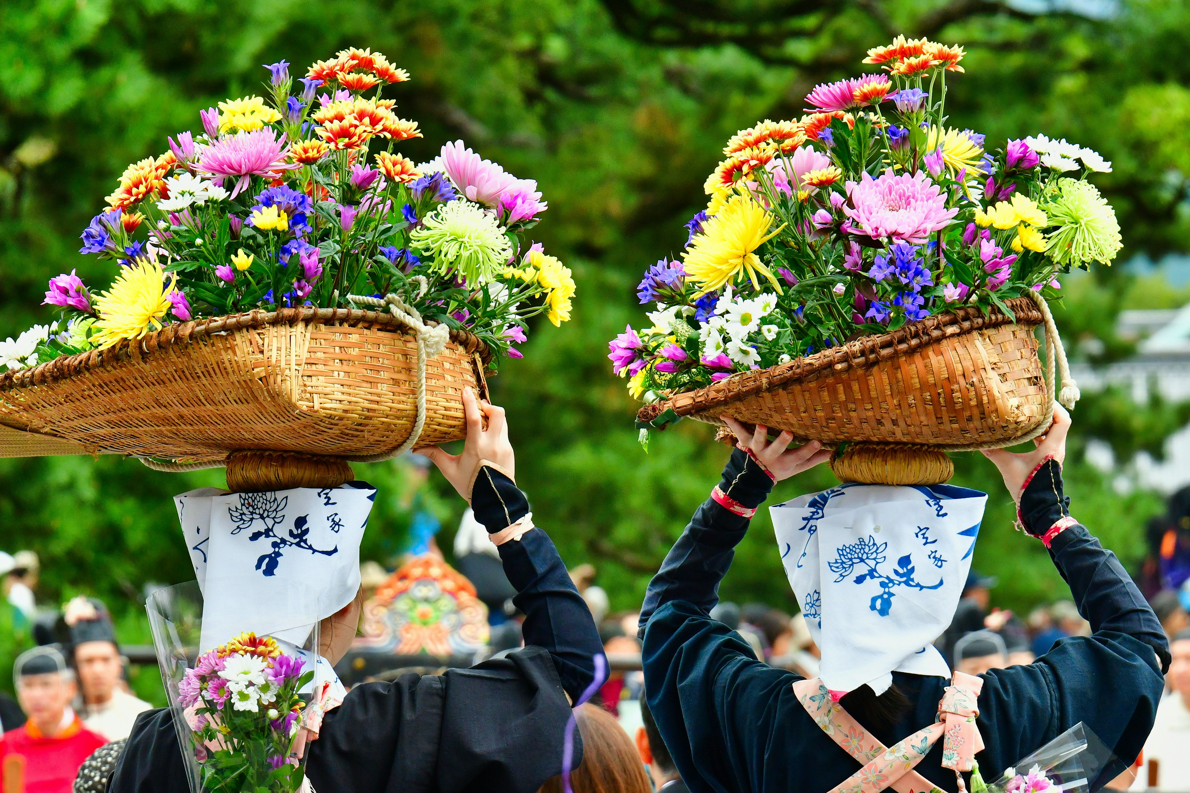 花を盛ったかごを頭に乗せた二人の女性が祭りの衣装で歩いている