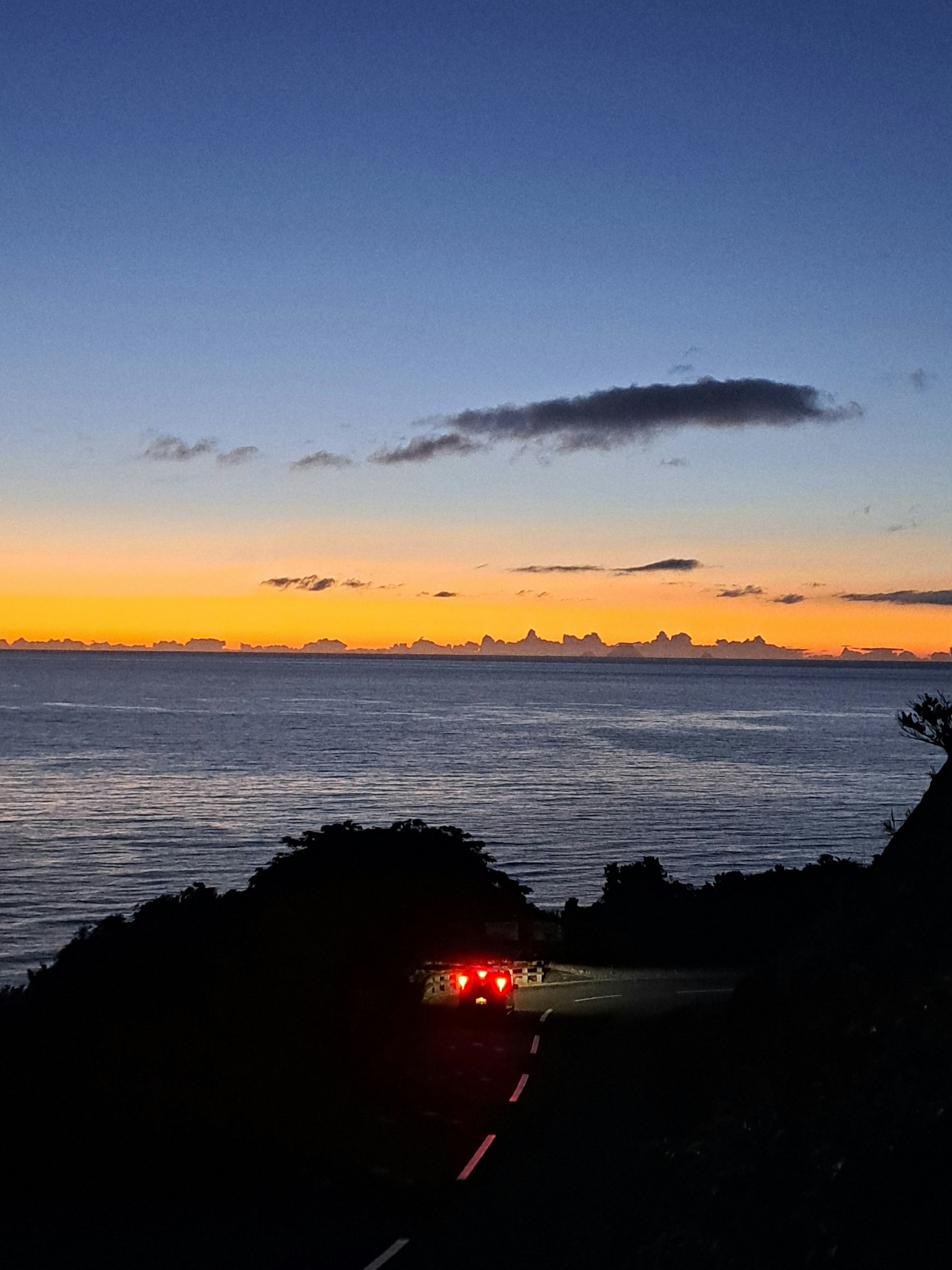 Winding road by the sunset ocean with car taillights