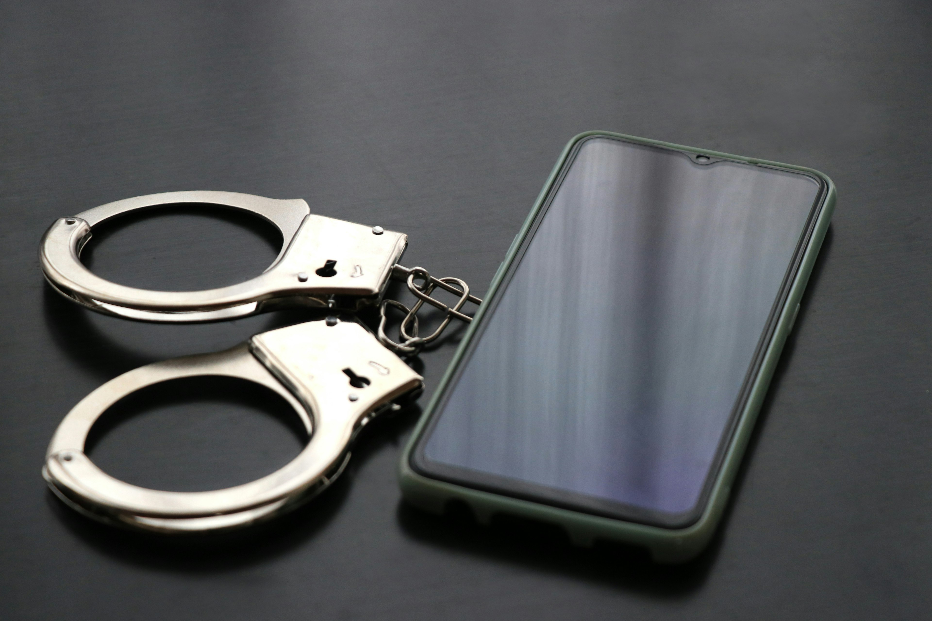 Handcuffs and a smartphone placed on a black background