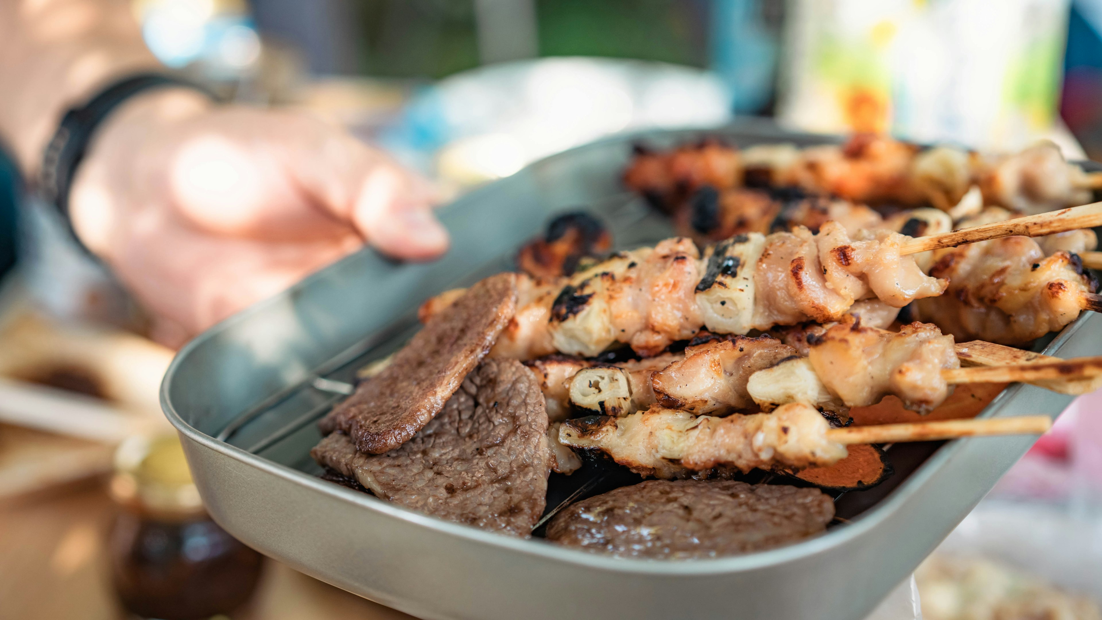 Hand, die ein Tablett mit verschiedenen Spießen und gegrilltem Fleisch hält