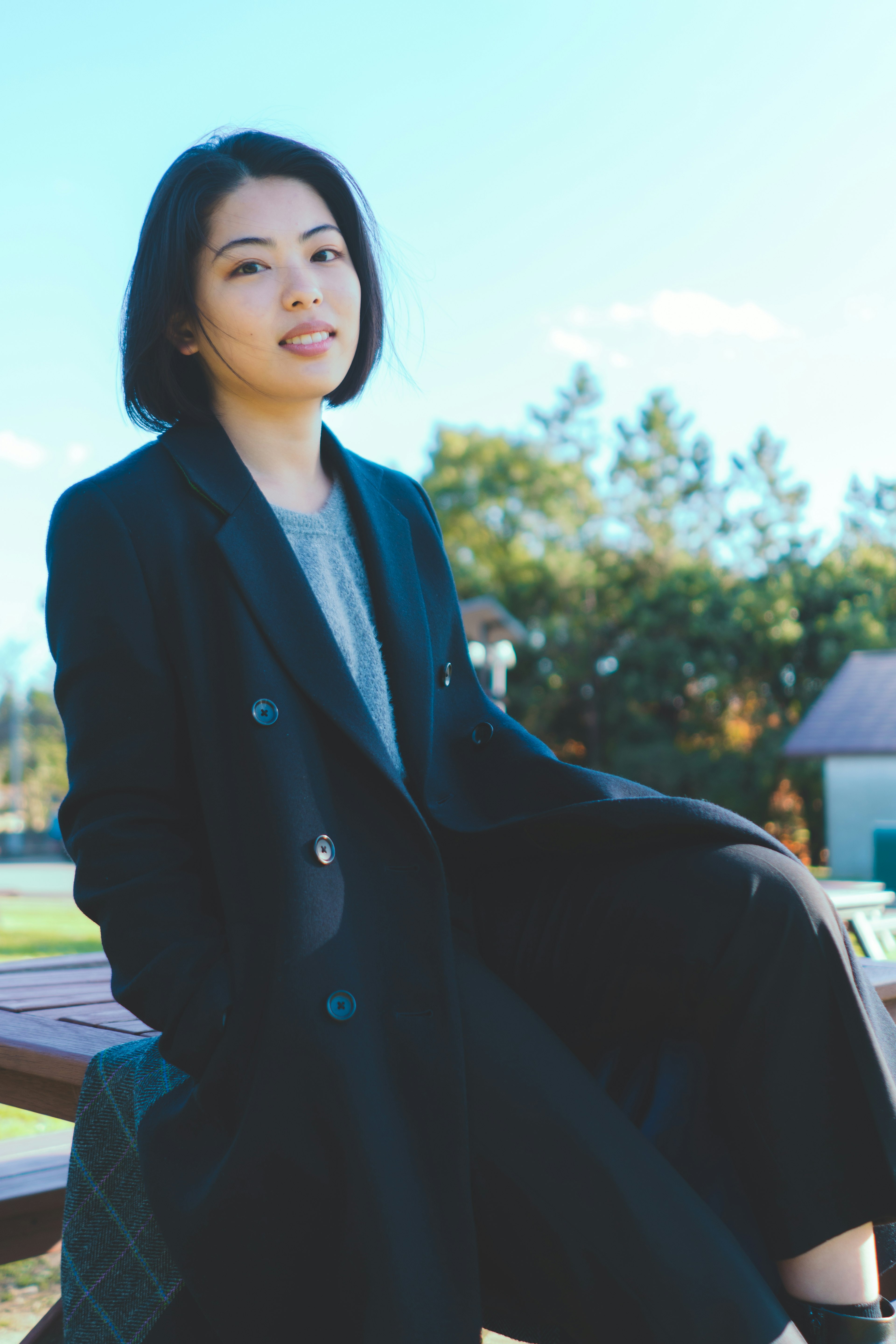 A woman sitting in a park wearing a black coat