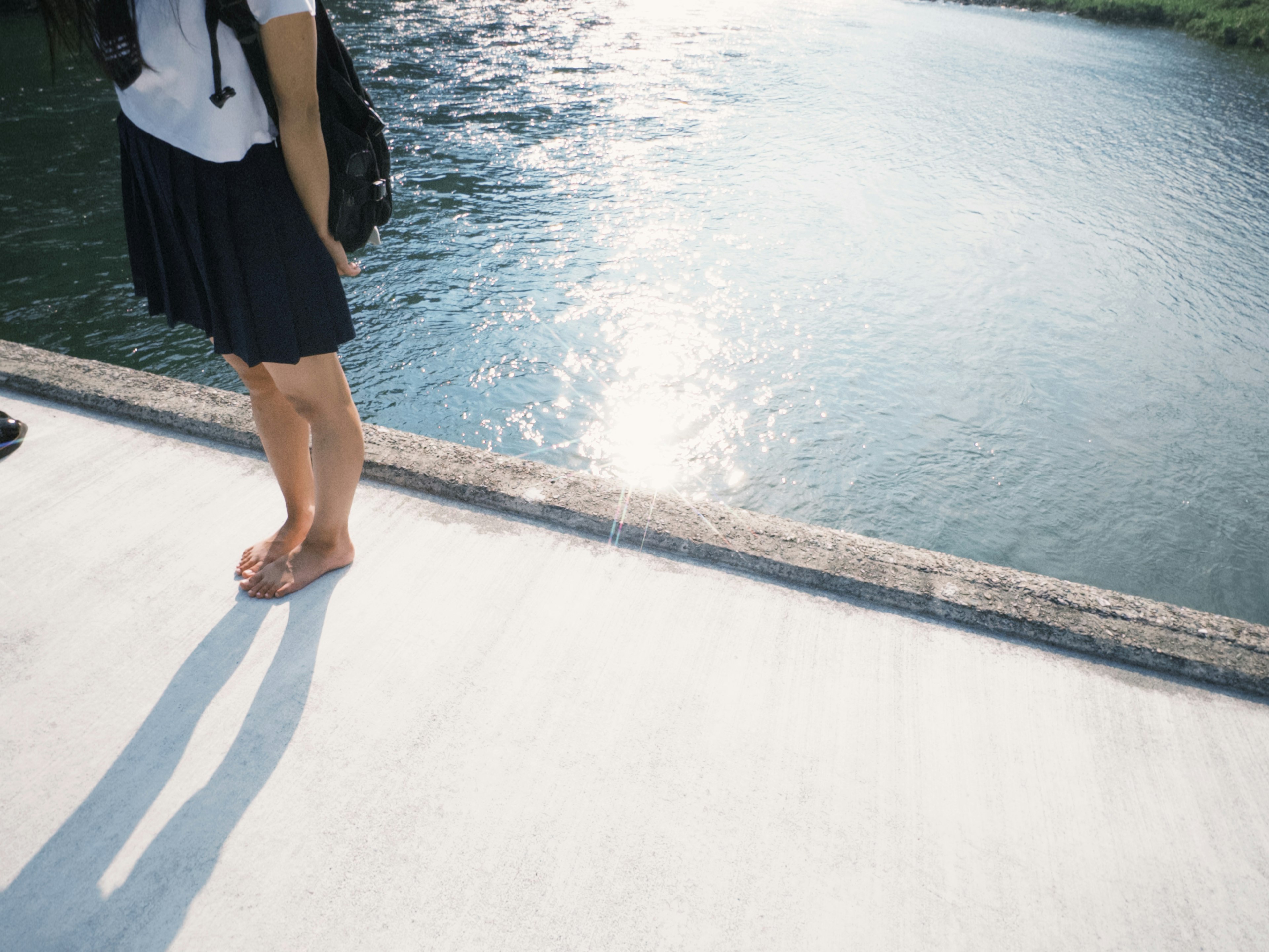 Une femme debout au bord de l'eau avec les pieds nus et des ombres