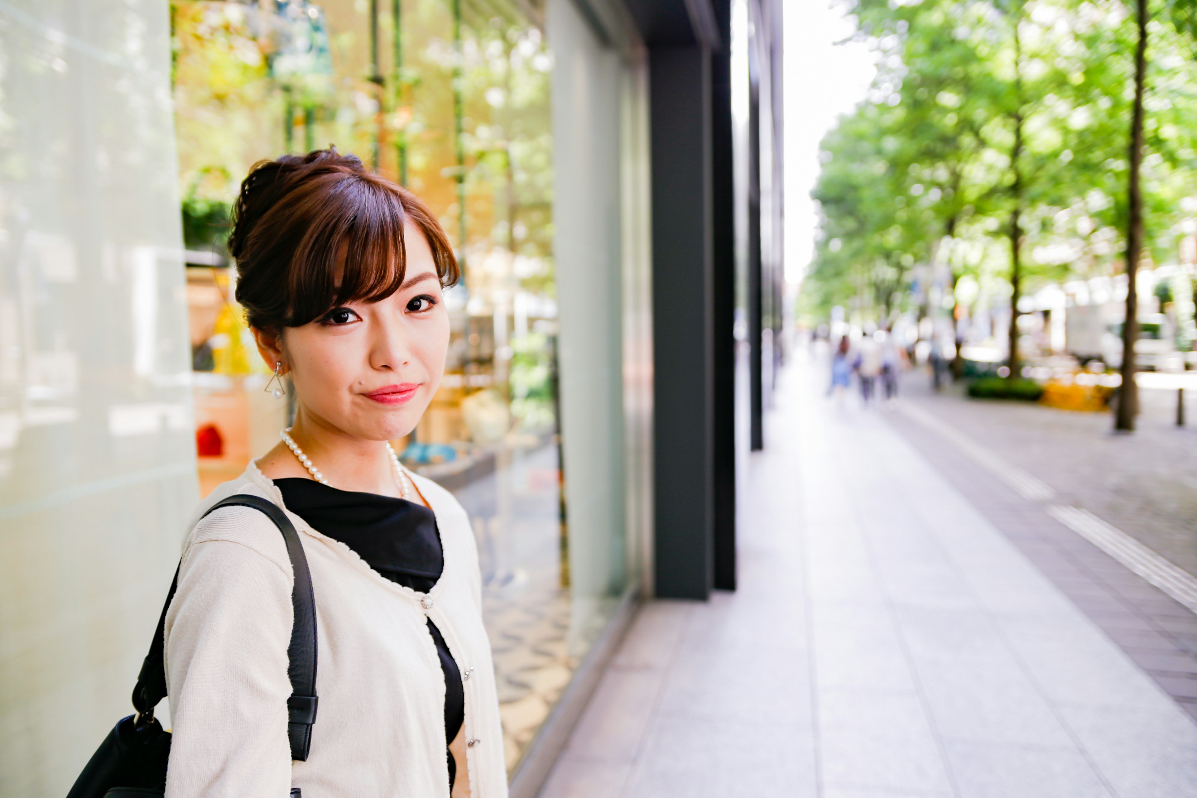 街の通りで微笑む女性のポートレート 背景には緑の木々と店舗の窓