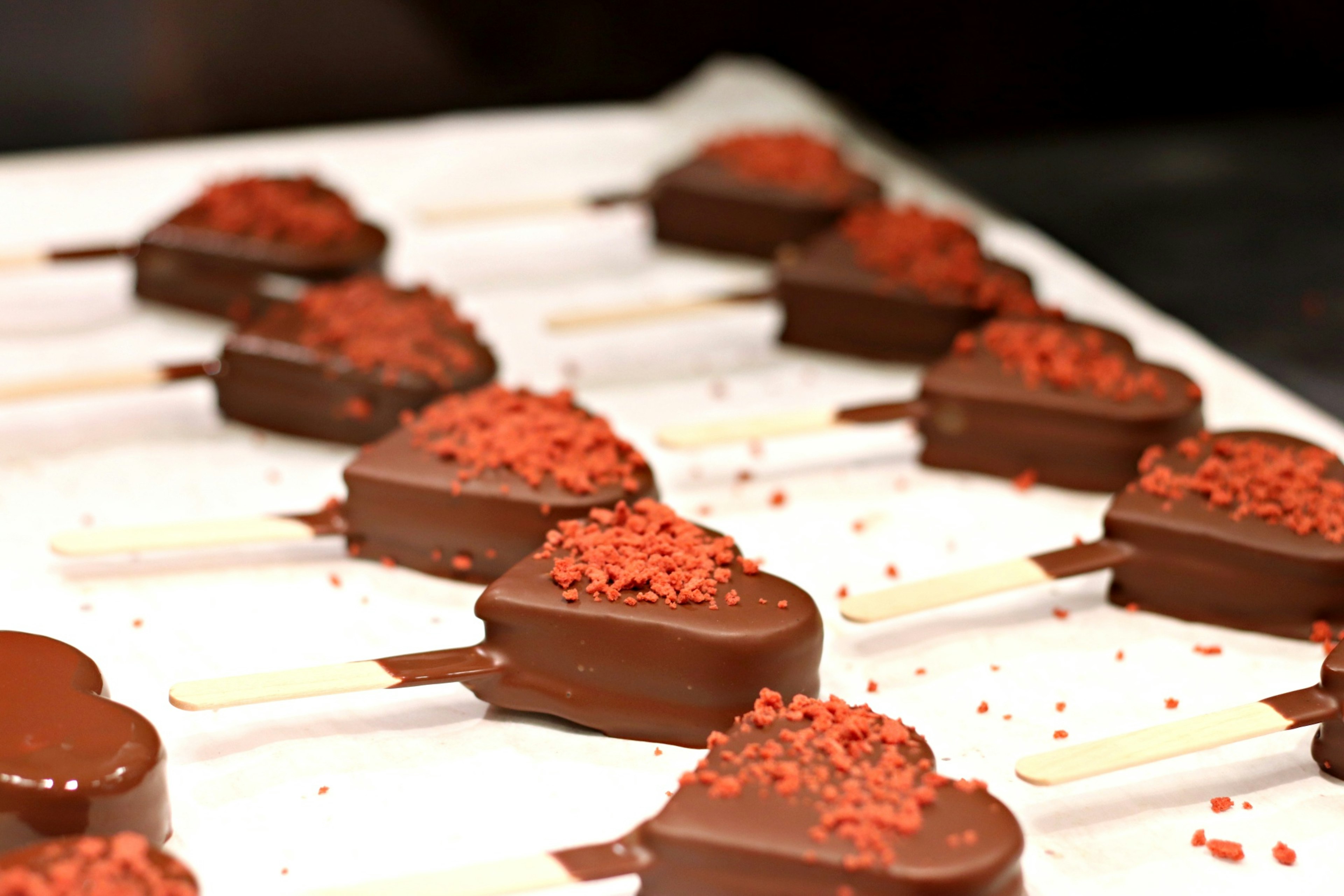 Heart-shaped chocolate-covered popsicles with red sprinkles arranged on a tray