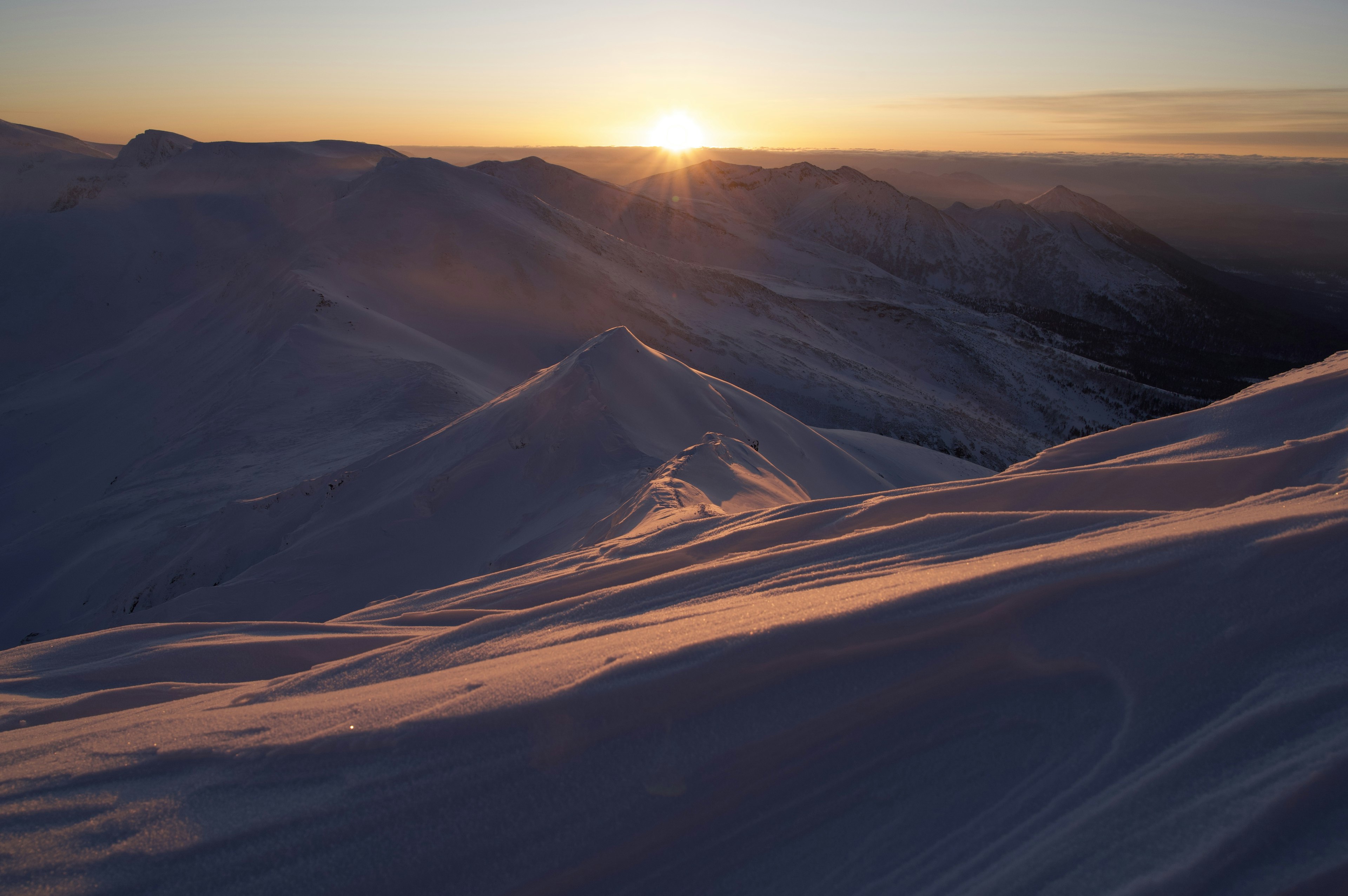 Montañas cubiertas de nieve con el sol saliendo al fondo