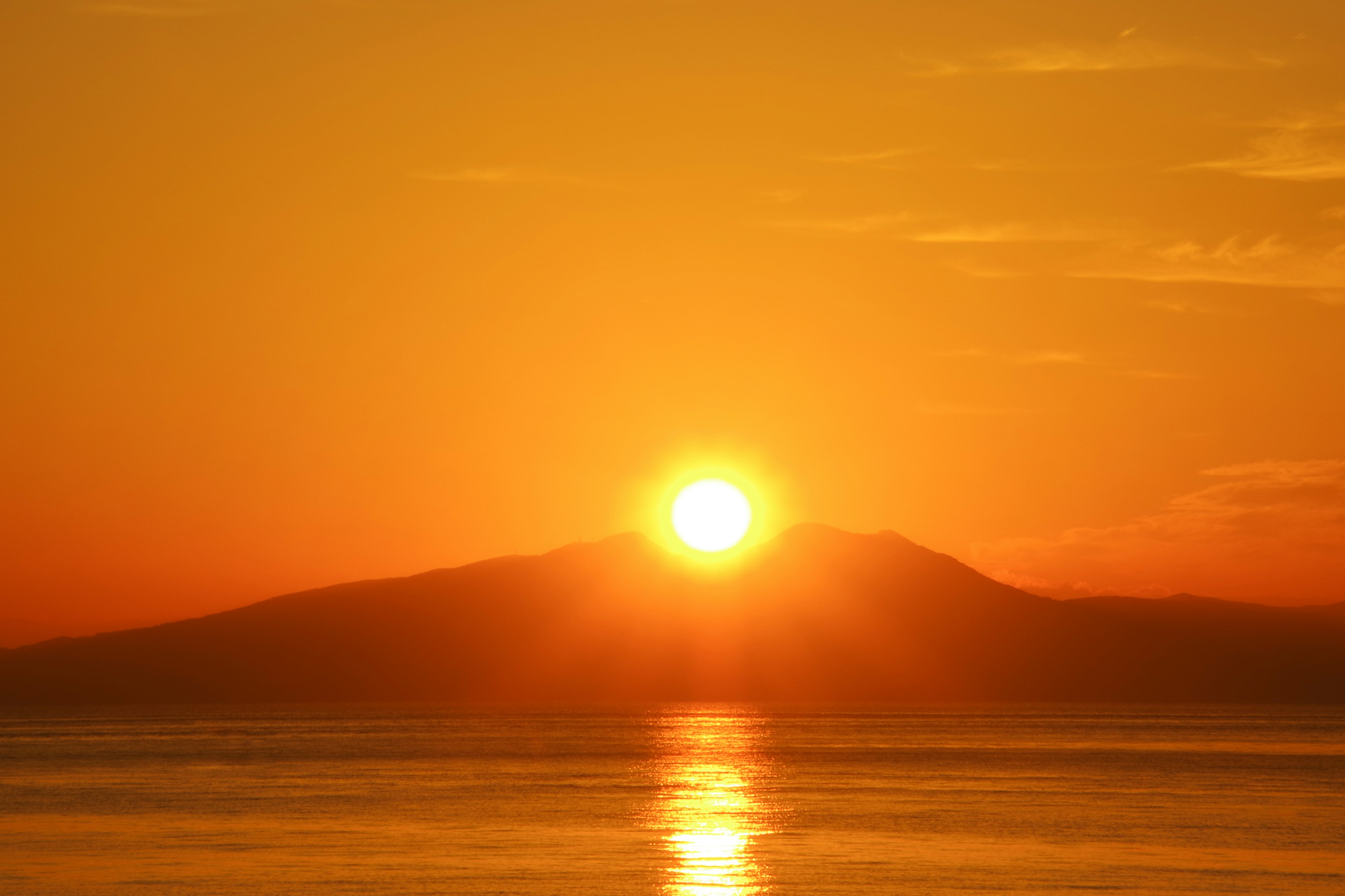 Una hermosa puesta de sol sobre una montaña con un cielo naranja y agua tranquila que refleja la luz