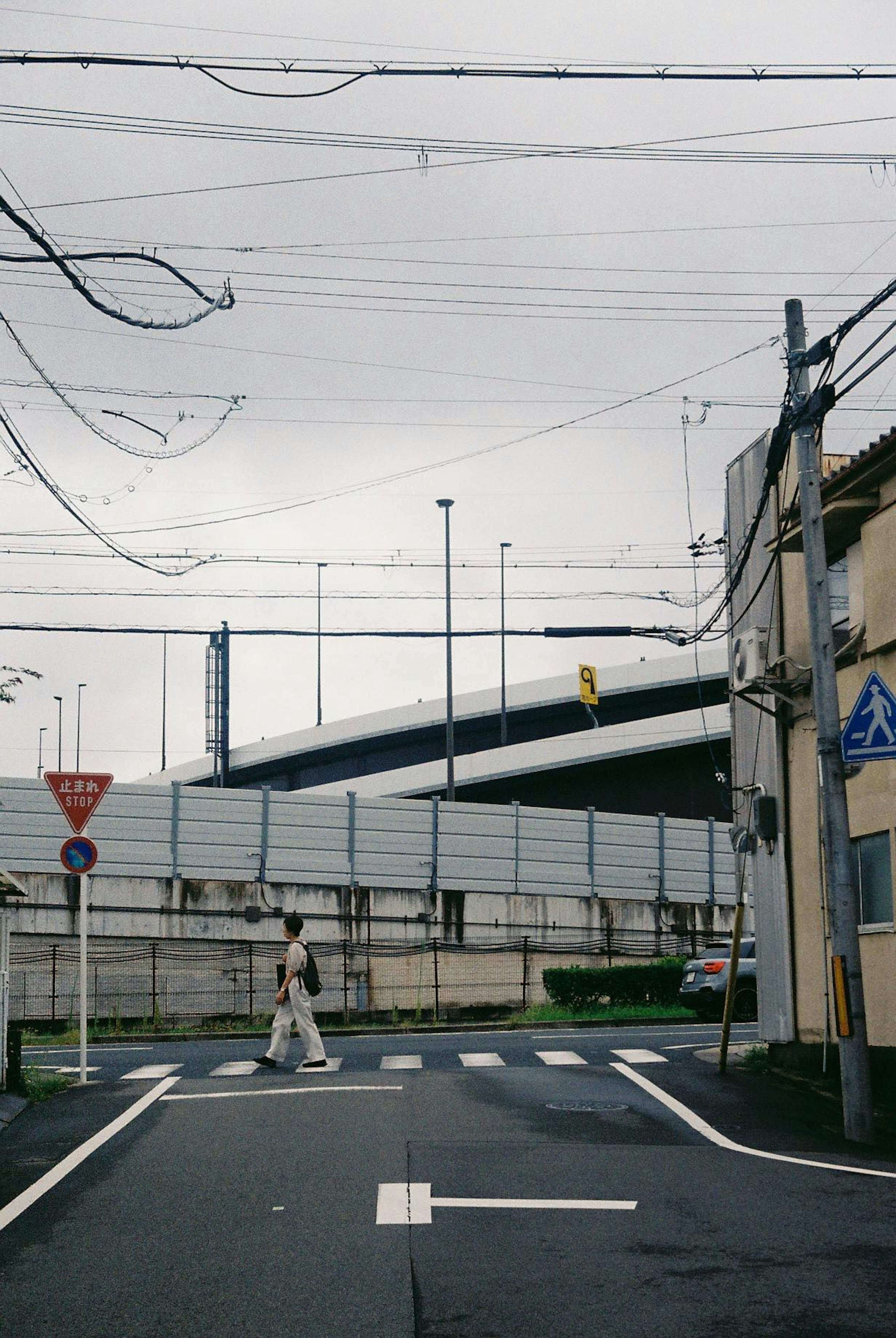 Una persona caminando en una intersección bajo un cielo nublado con estructuras de puente visibles