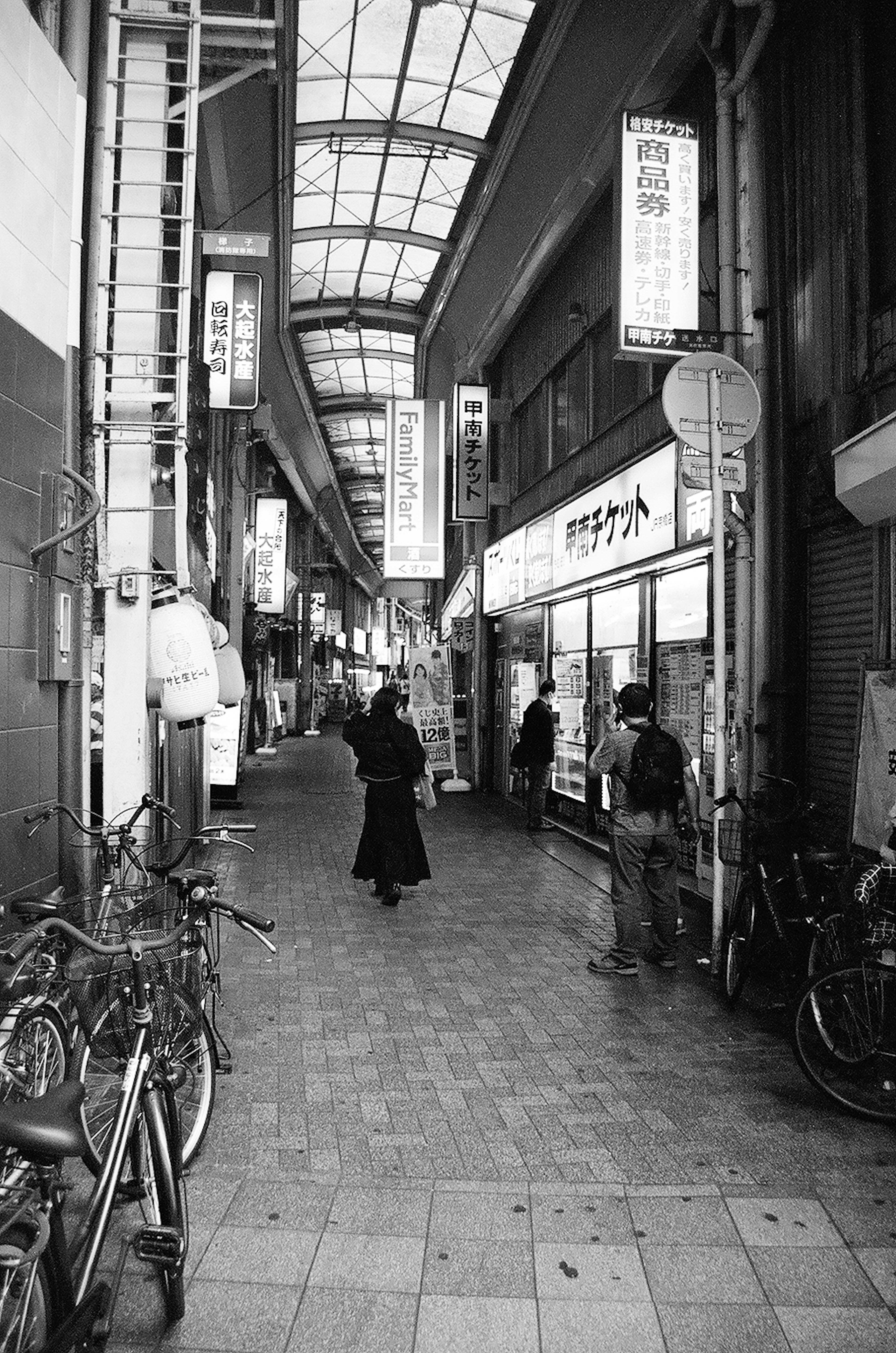 Escena de calle en blanco y negro en un arcade comercial con personas bicicletas y letreros