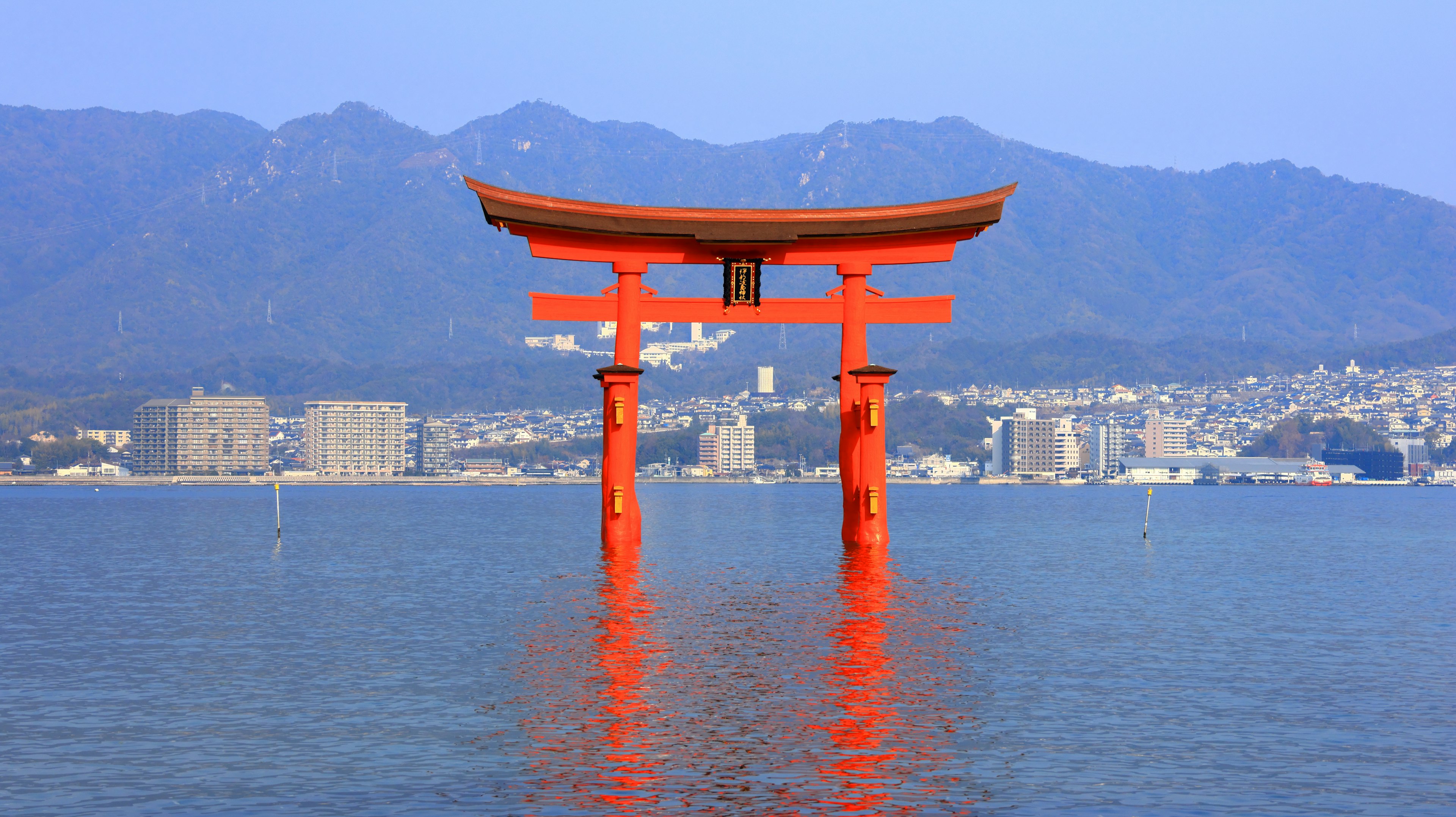 Gerbang torii merah berdiri di air dengan latar belakang gunung biru