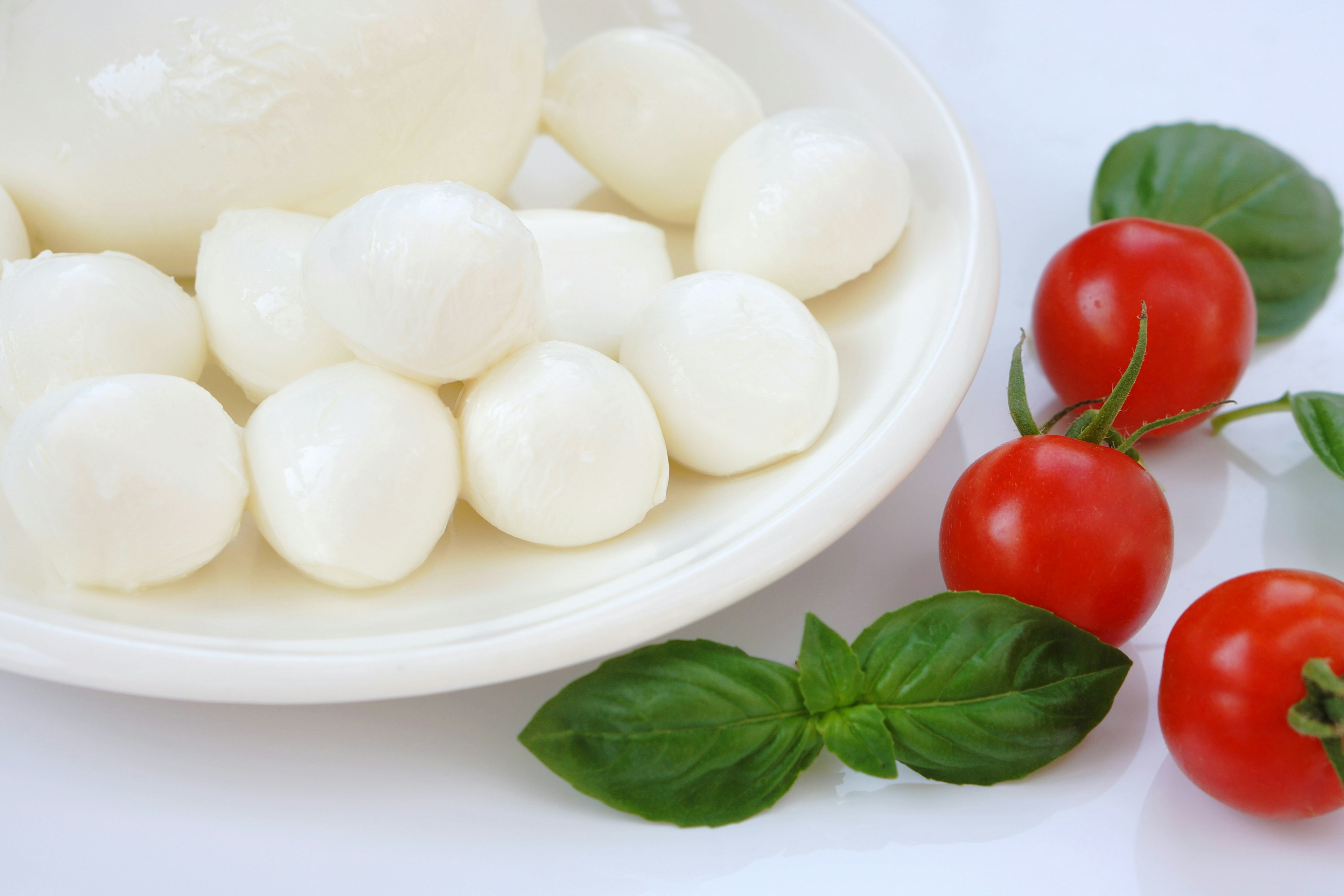 Palline di mozzarella fresca e pomodorini su un piatto con foglie di basilico