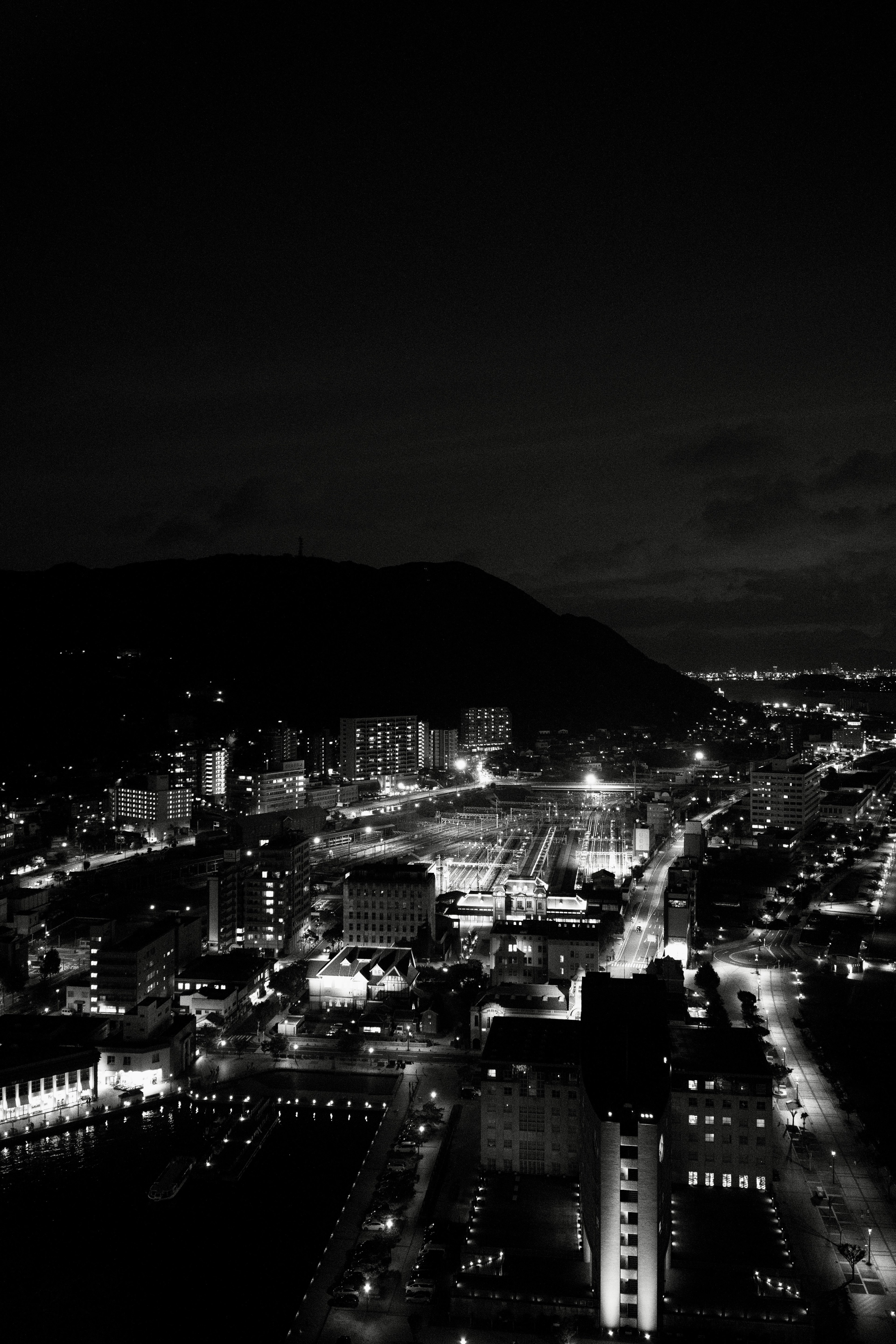 Panorama nocturno de la ciudad con edificios iluminados y silueta de montaña