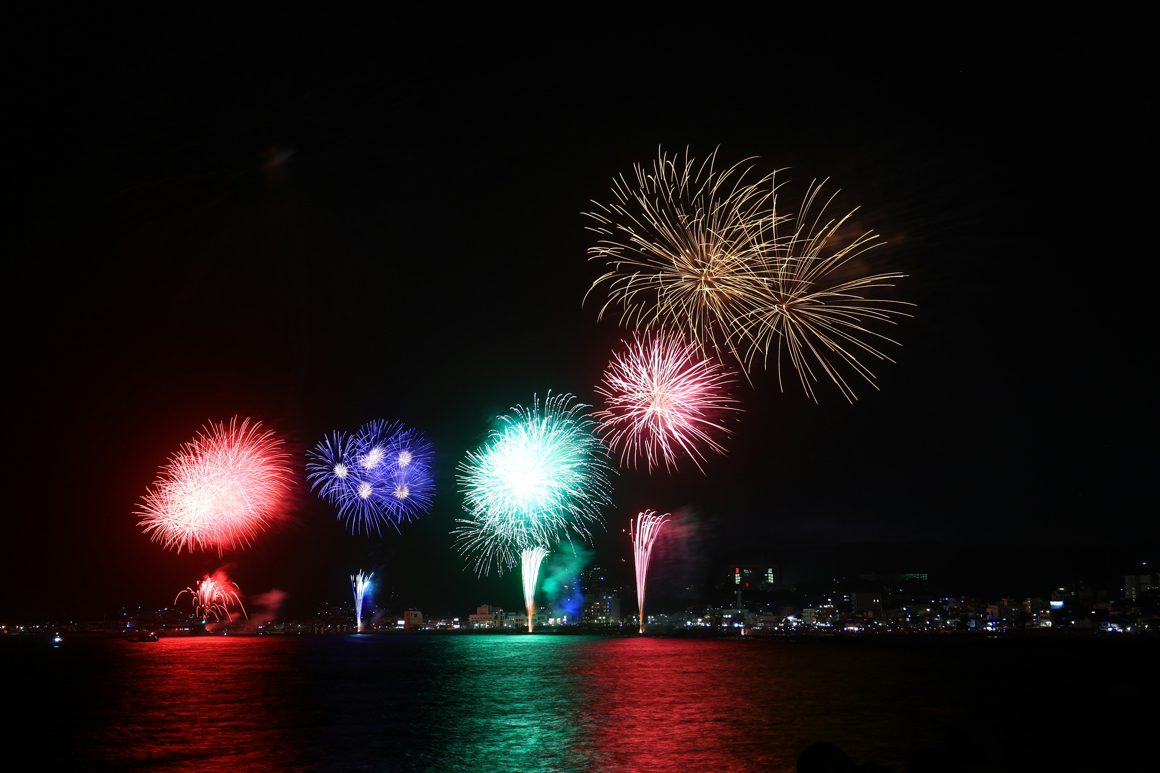 夜空に打ち上げられるカラフルな花火と水面に映る光