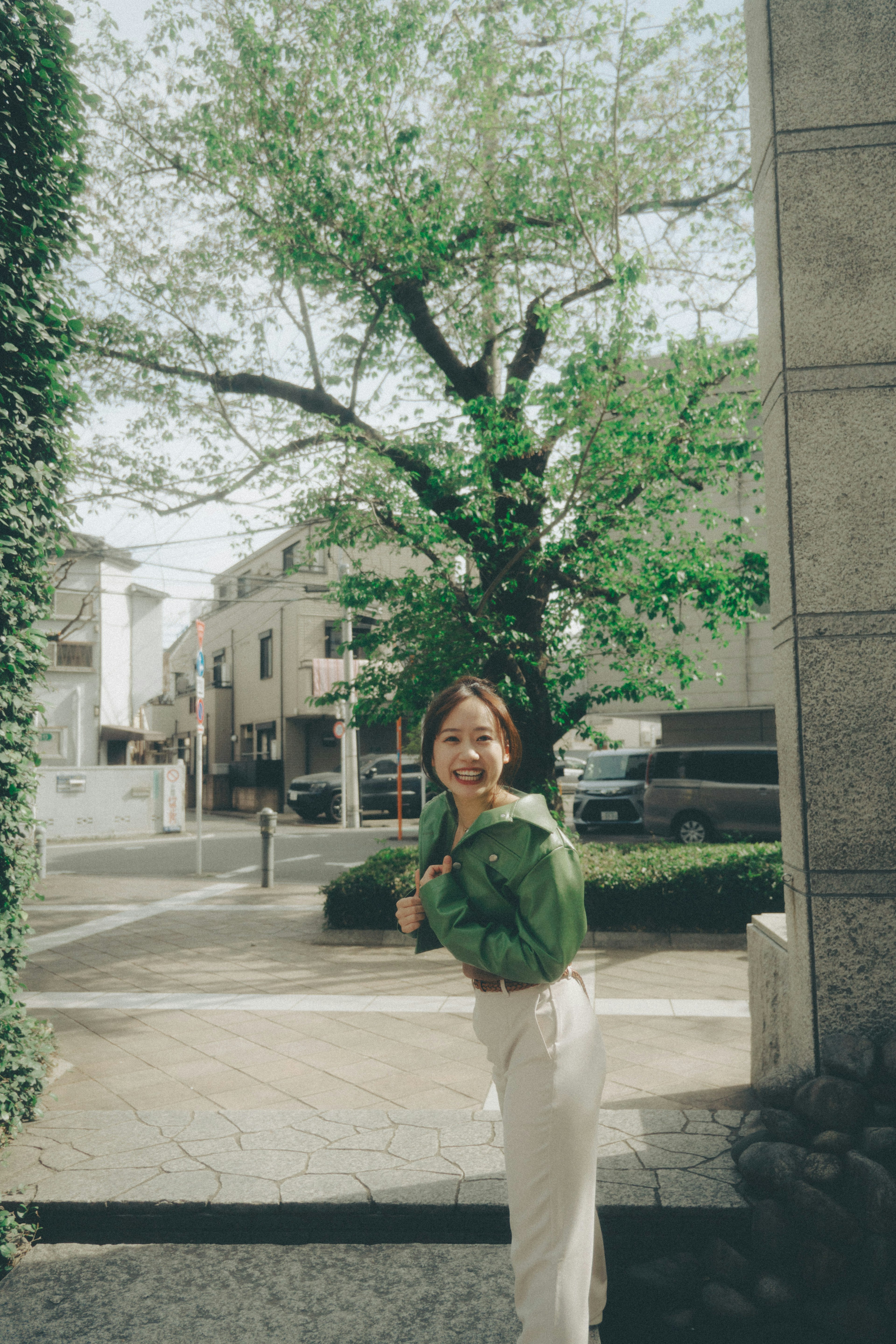 A smiling woman holding green leaves in a street corner setting