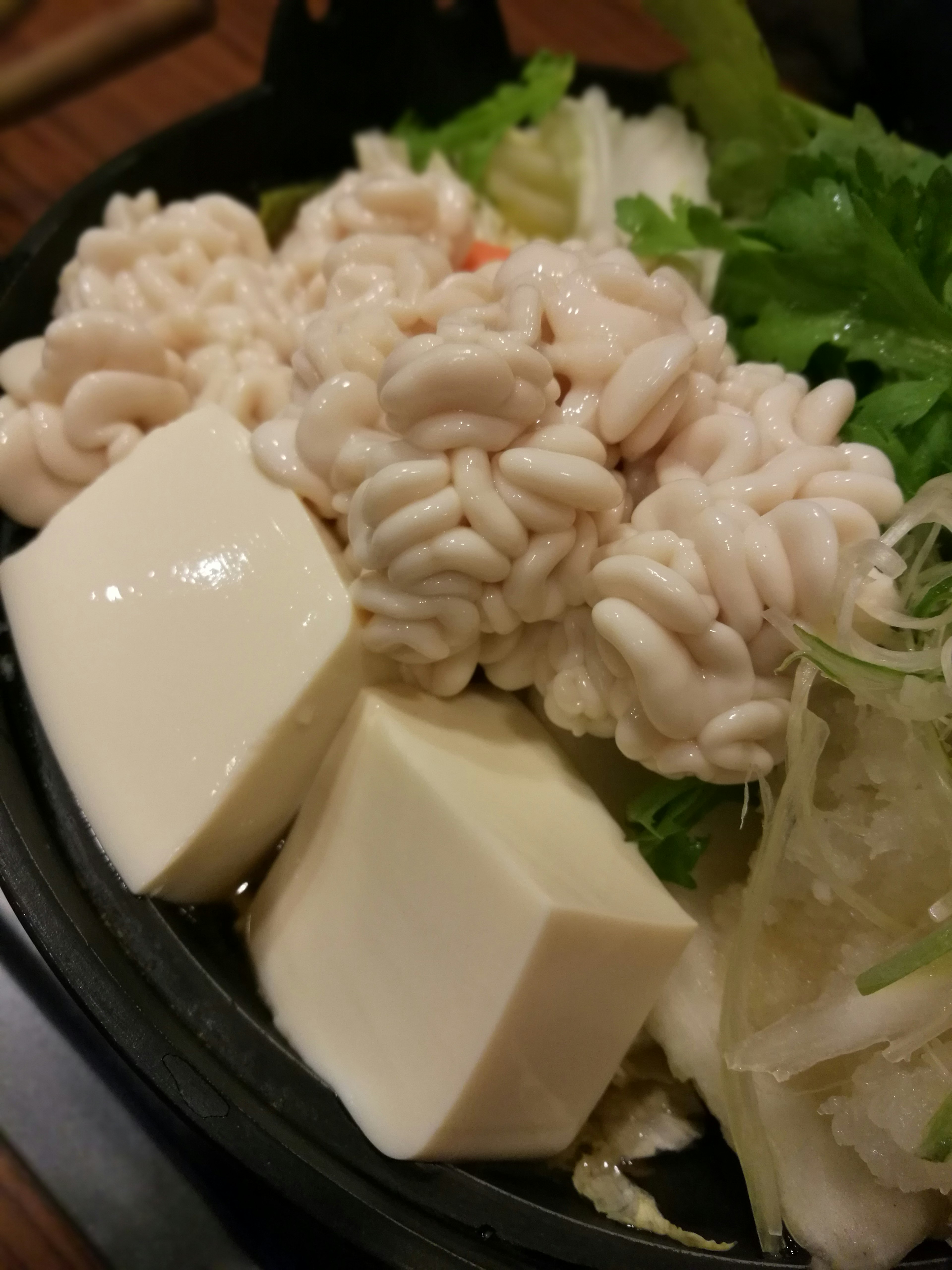 A bowl of hot pot featuring white tofu and thinly sliced ingredients