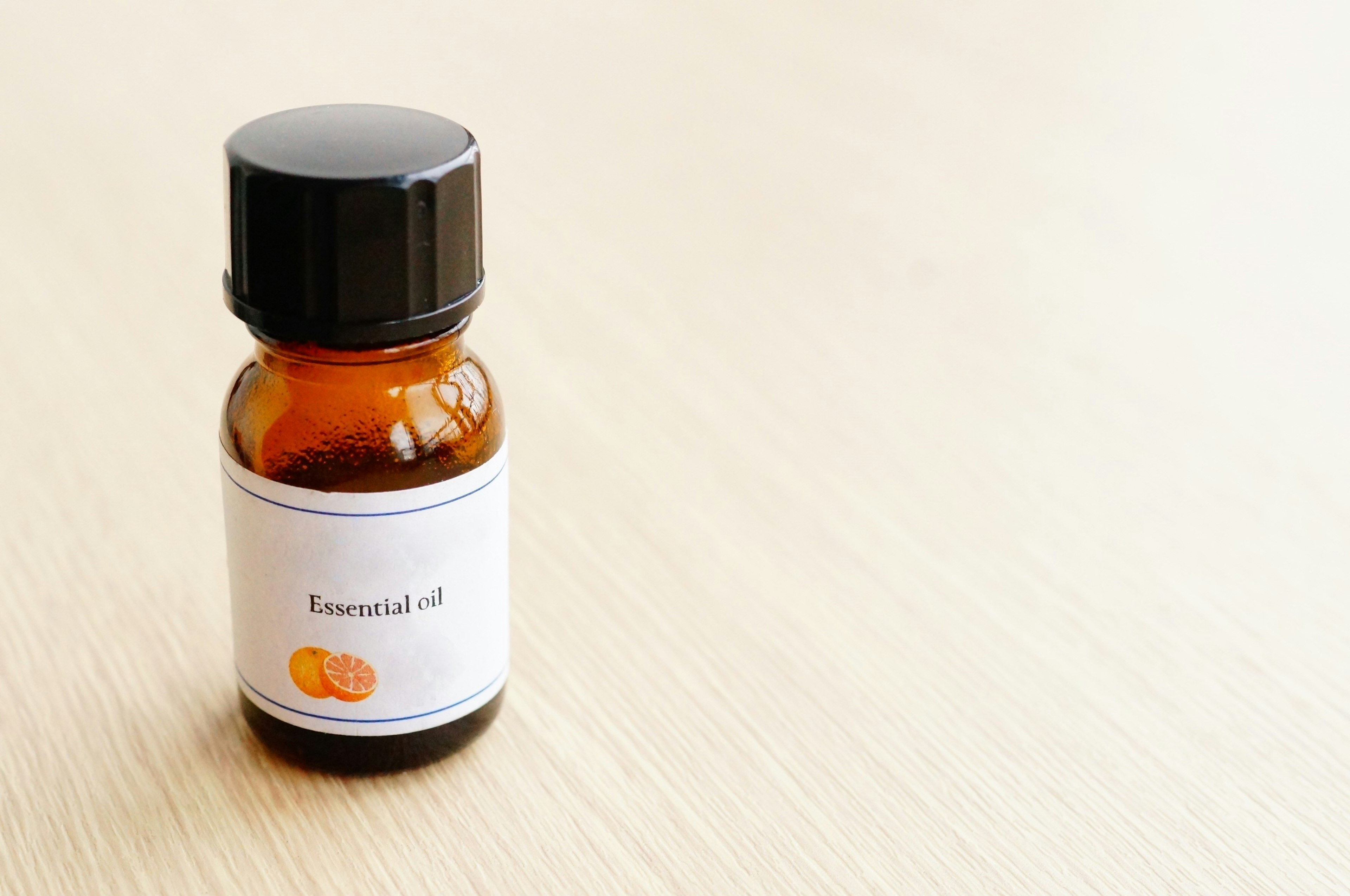 Brown essential oil bottle with orange label on a light wooden surface