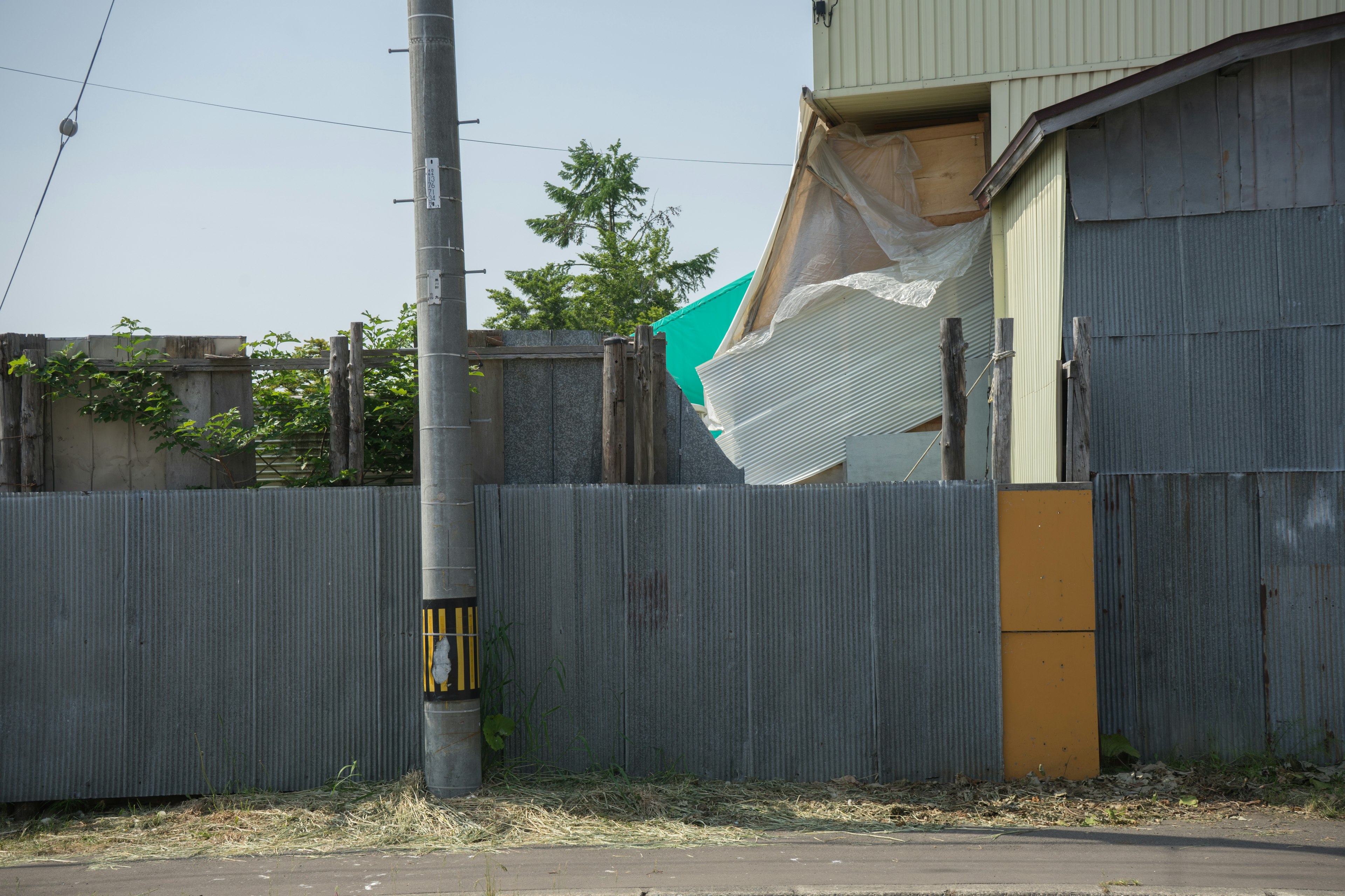 Landscape featuring a building covered with a blue tarp and a gray fence